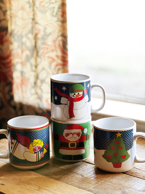 Set of four Christmas-themed mugs on a wooden surface with a window in the background.