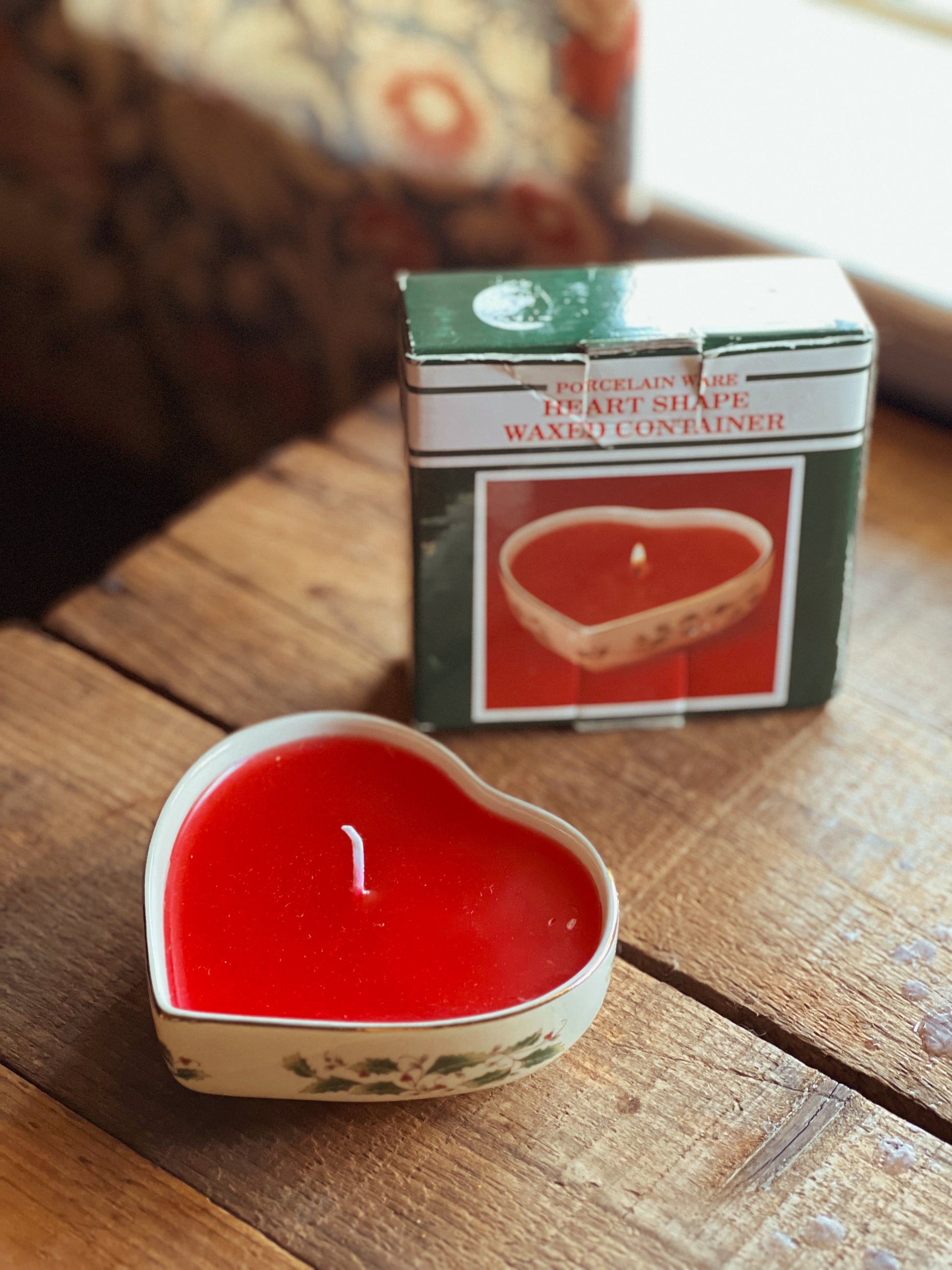 Heart-shaped red candle on a wooden surface with its packaging in the background.