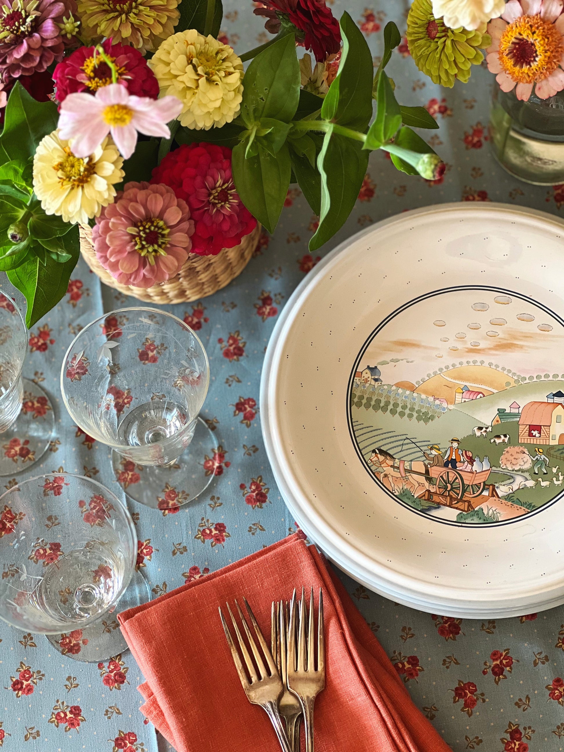 Vintage dinner plate with a farm scene in the center. The plate is blue and white and the scene is in pastel colors.