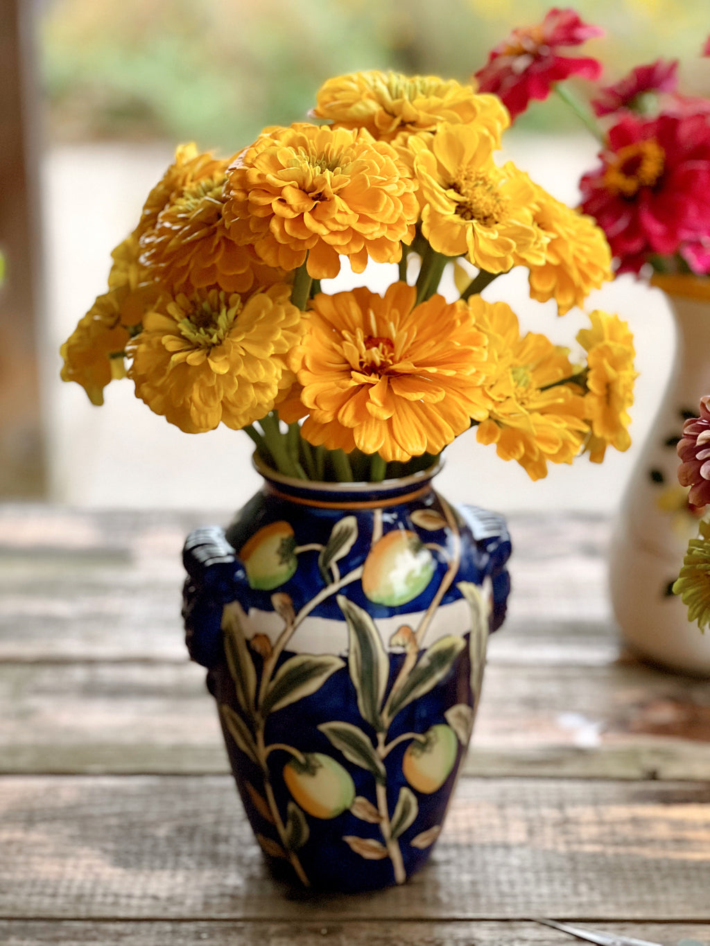 Navy blue vase hand painted with yellow lemons and filled with yellow zinnias