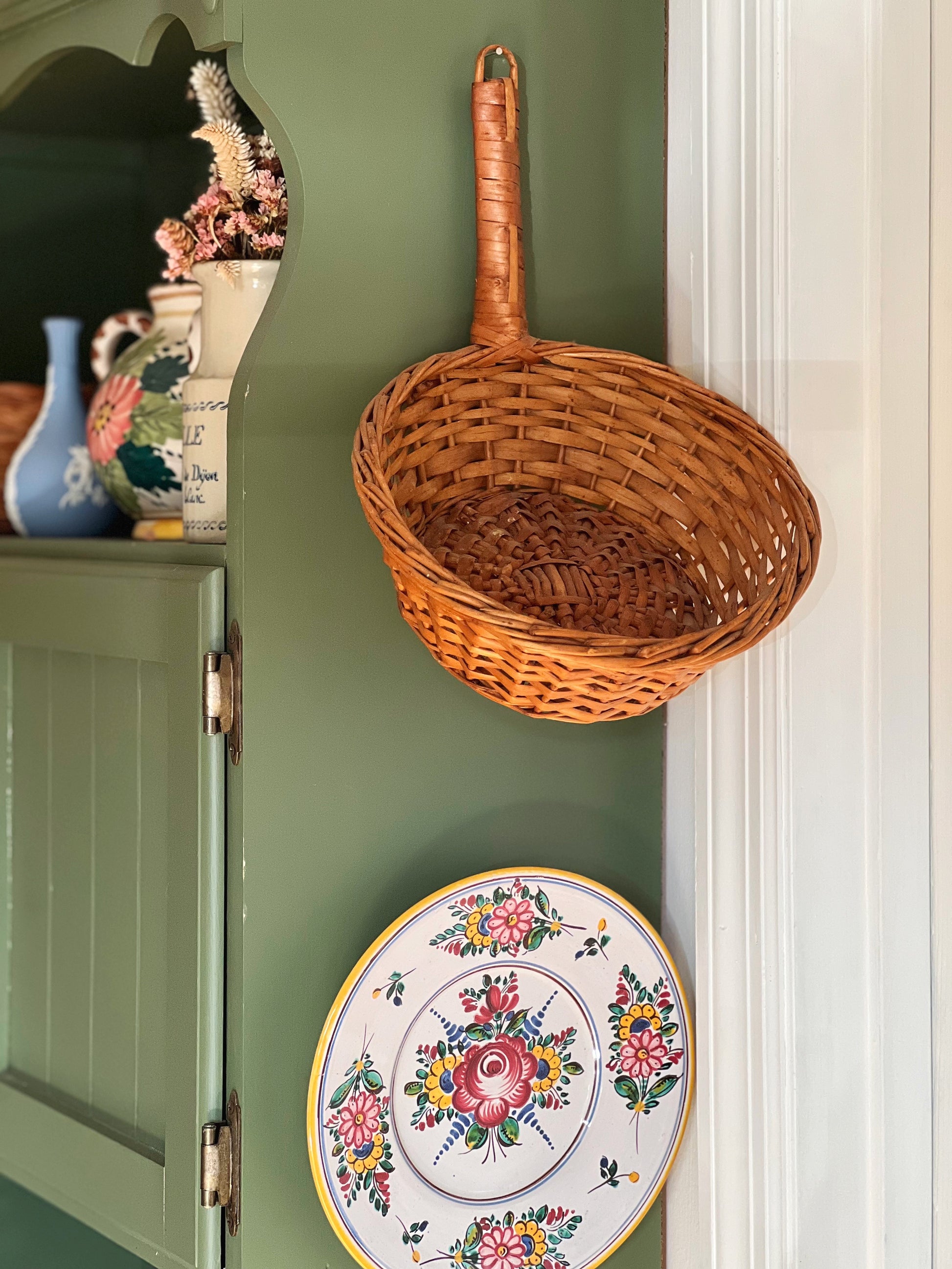 Vintage round basket with a handle that is hung on the side of a cabinet