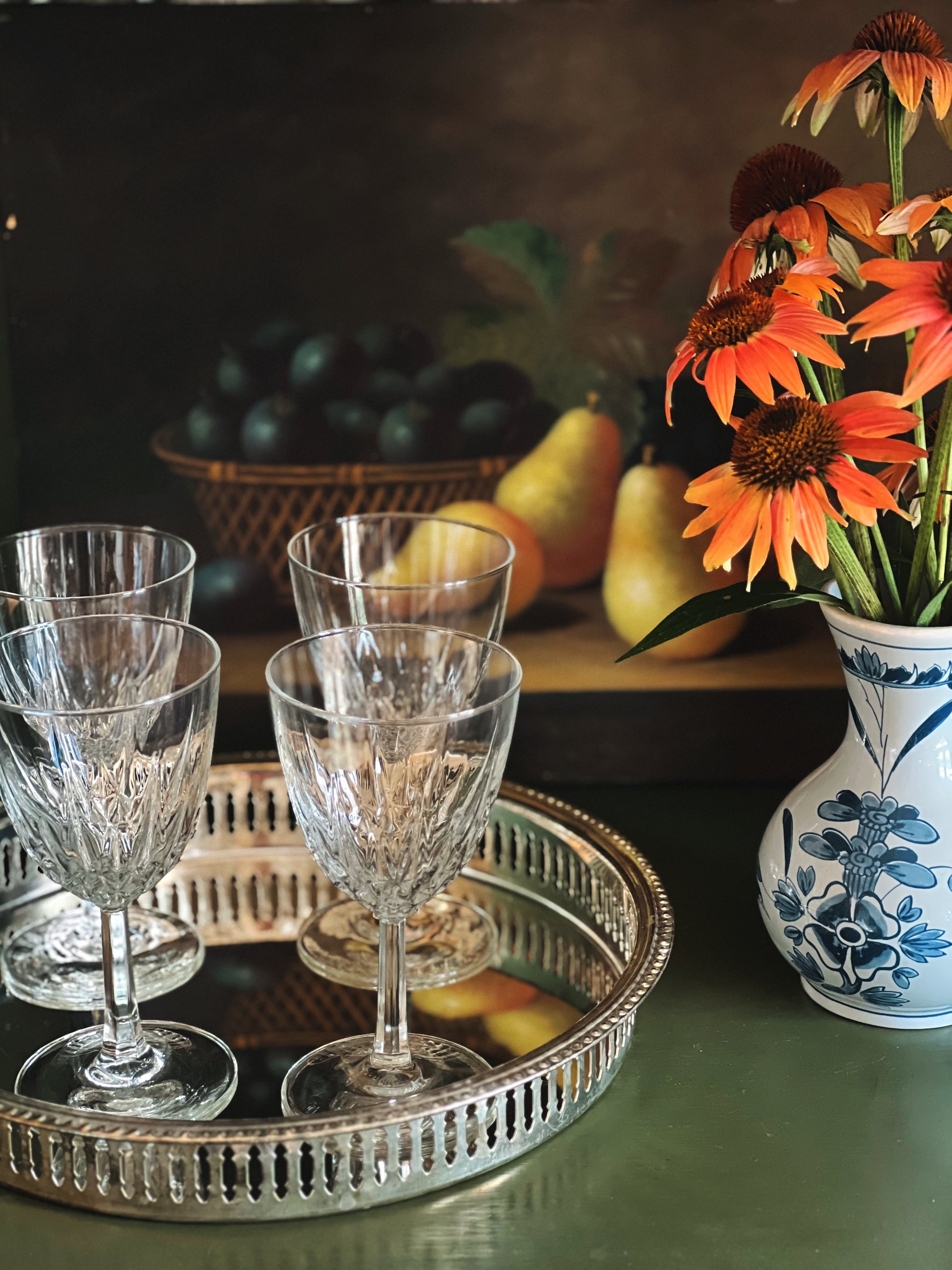 Tray with crystal glasses, fruit, and a vase with flowers on a table.