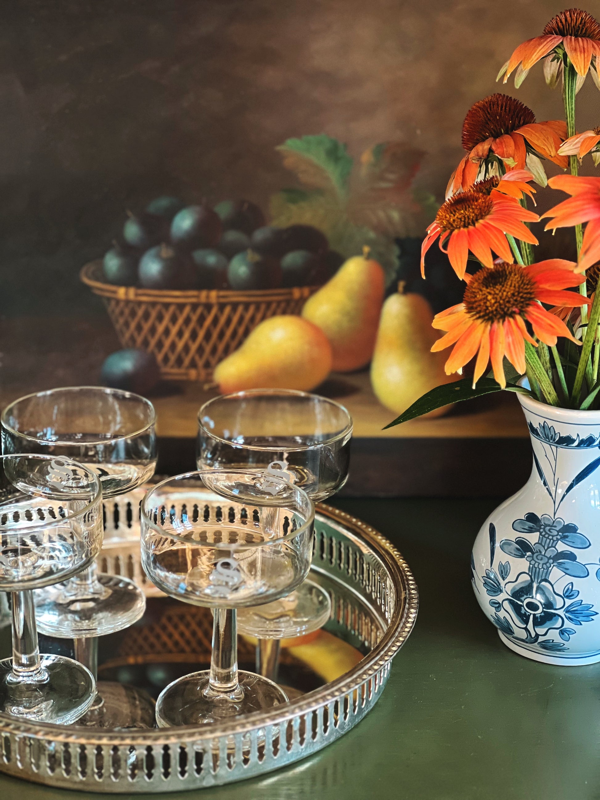 Still life with glasses, pears, plums, and flowers on a table.
