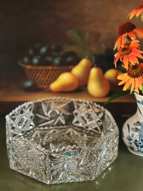 Decorative crystal bowl with intricate designs on a table with fruits and flowers.