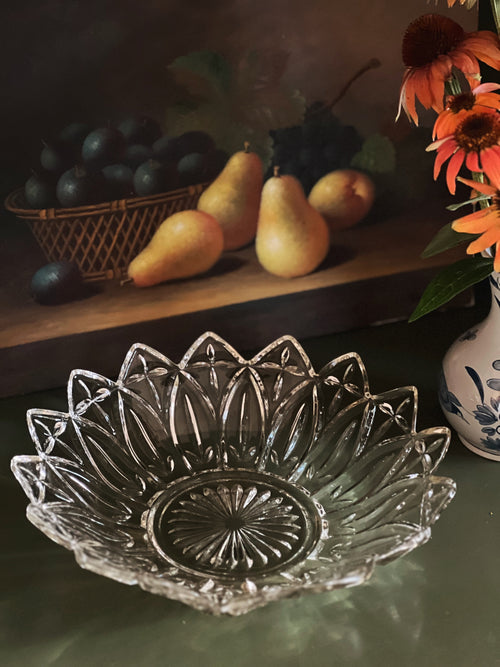Clear glass bowl with decorative design on a table with fruits and flowers.