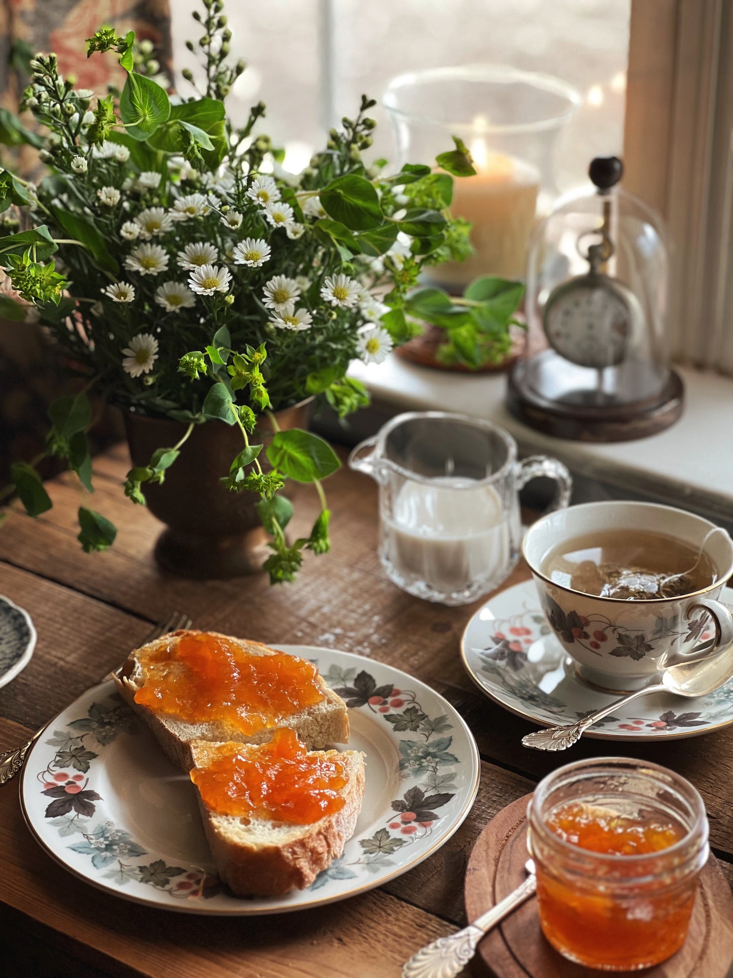 breakfast table with teacup & saucer, plate, creamer, floral arrangement and jar of jam