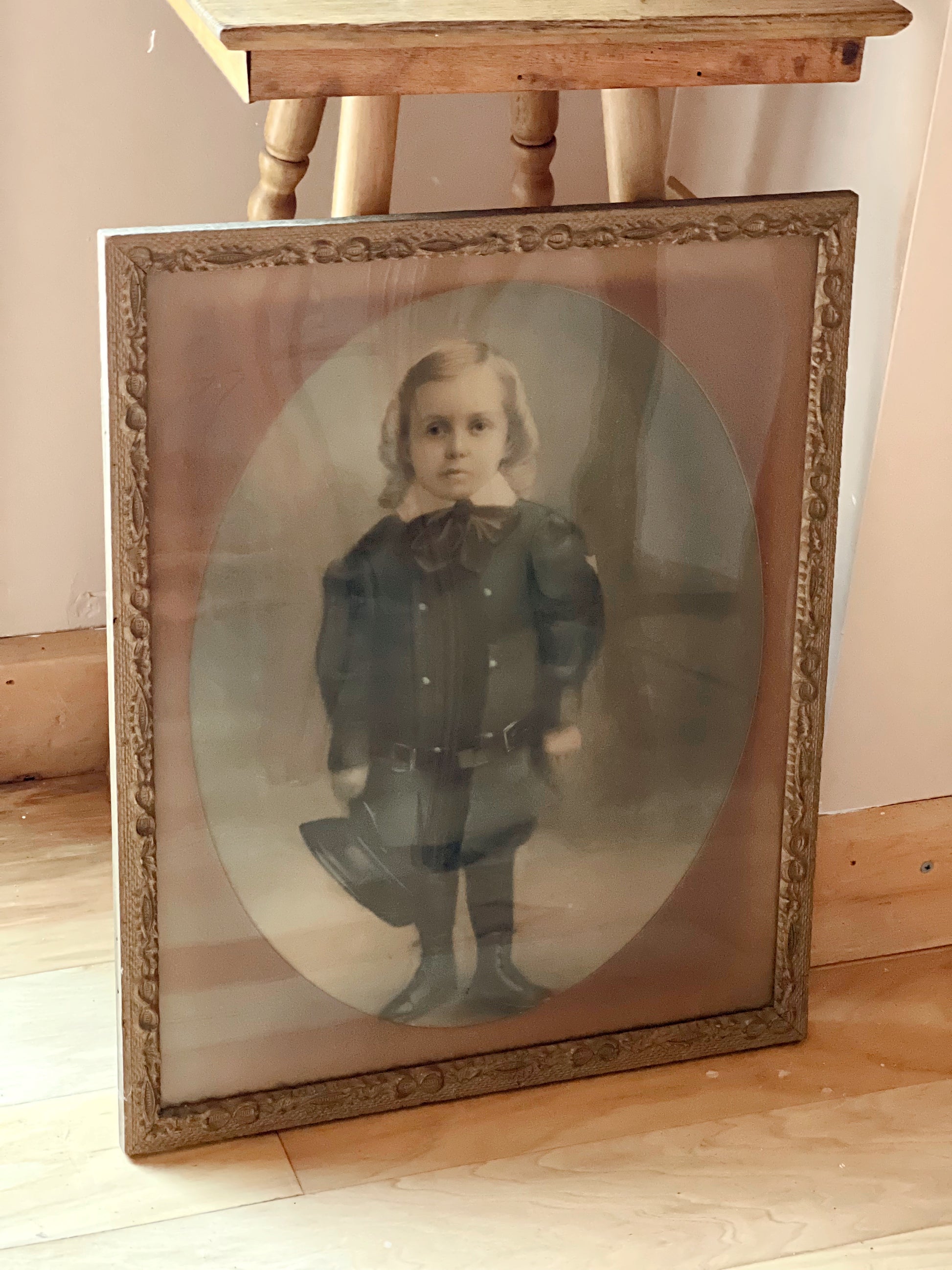Vintage photograph of a child in a ornate frame on a wooden floor.