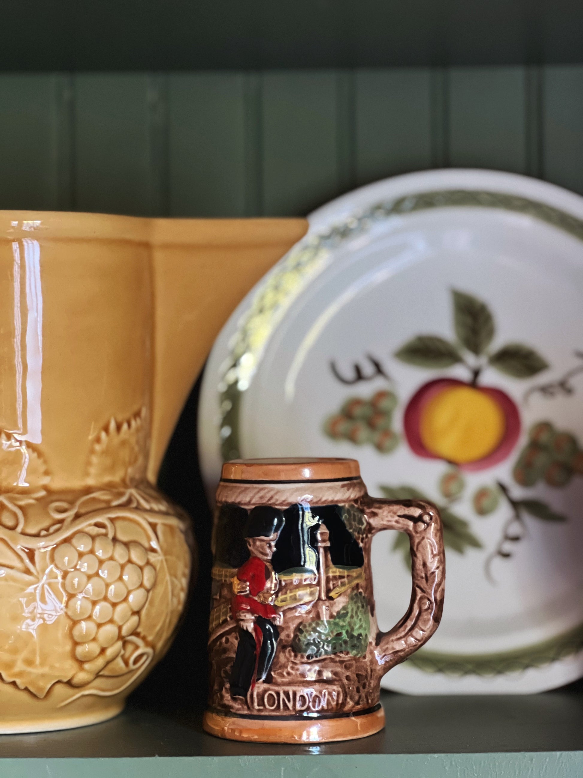 Ceramic mug with a decorative design, yellow vase, and patterned plate on a dark surface.