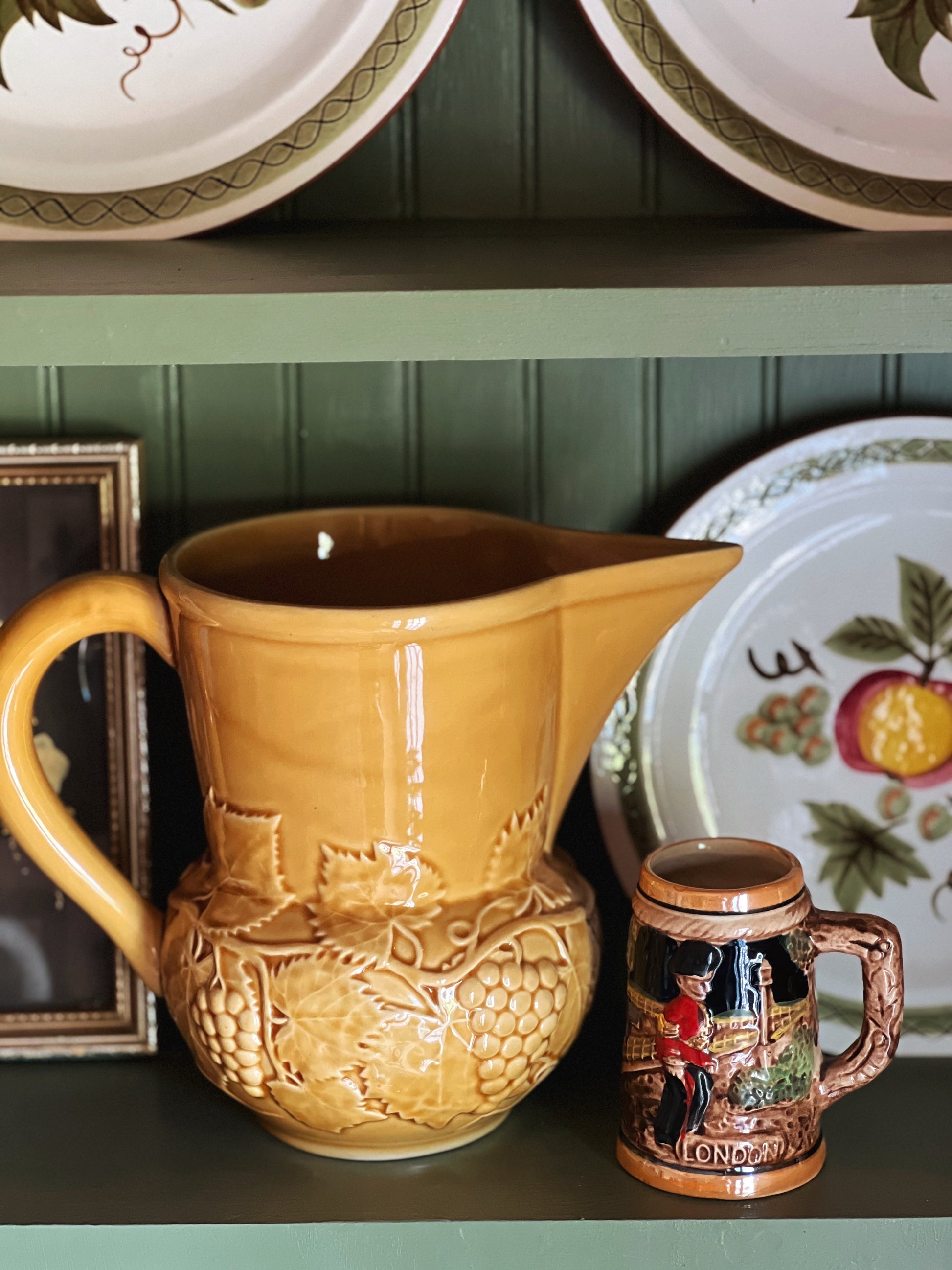 Ceramic pitcher and mug on a shelf with decorative plates in the background.