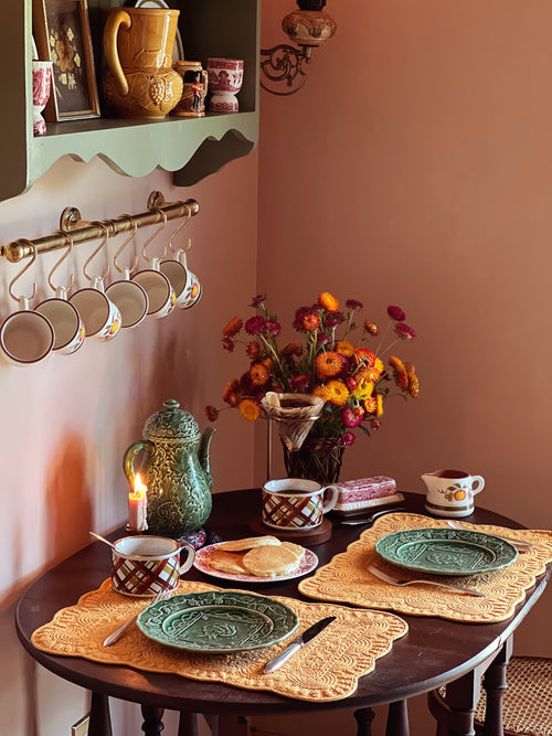 Dining table with ceramic plates, teapots, and a vase of flowers against a wall.