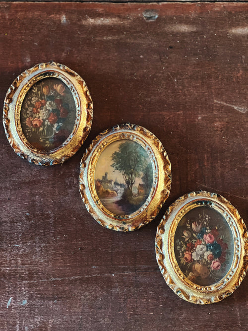 Three round paintings in ornate gold frames on a wooden surface