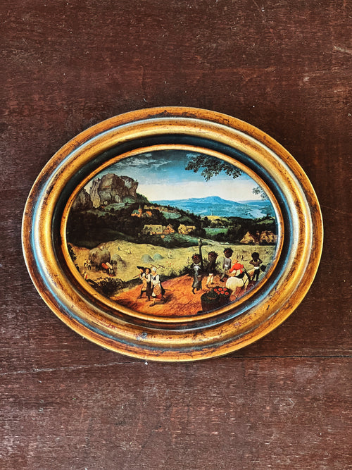 Small oval painting of a landscape with people on a wooden surface