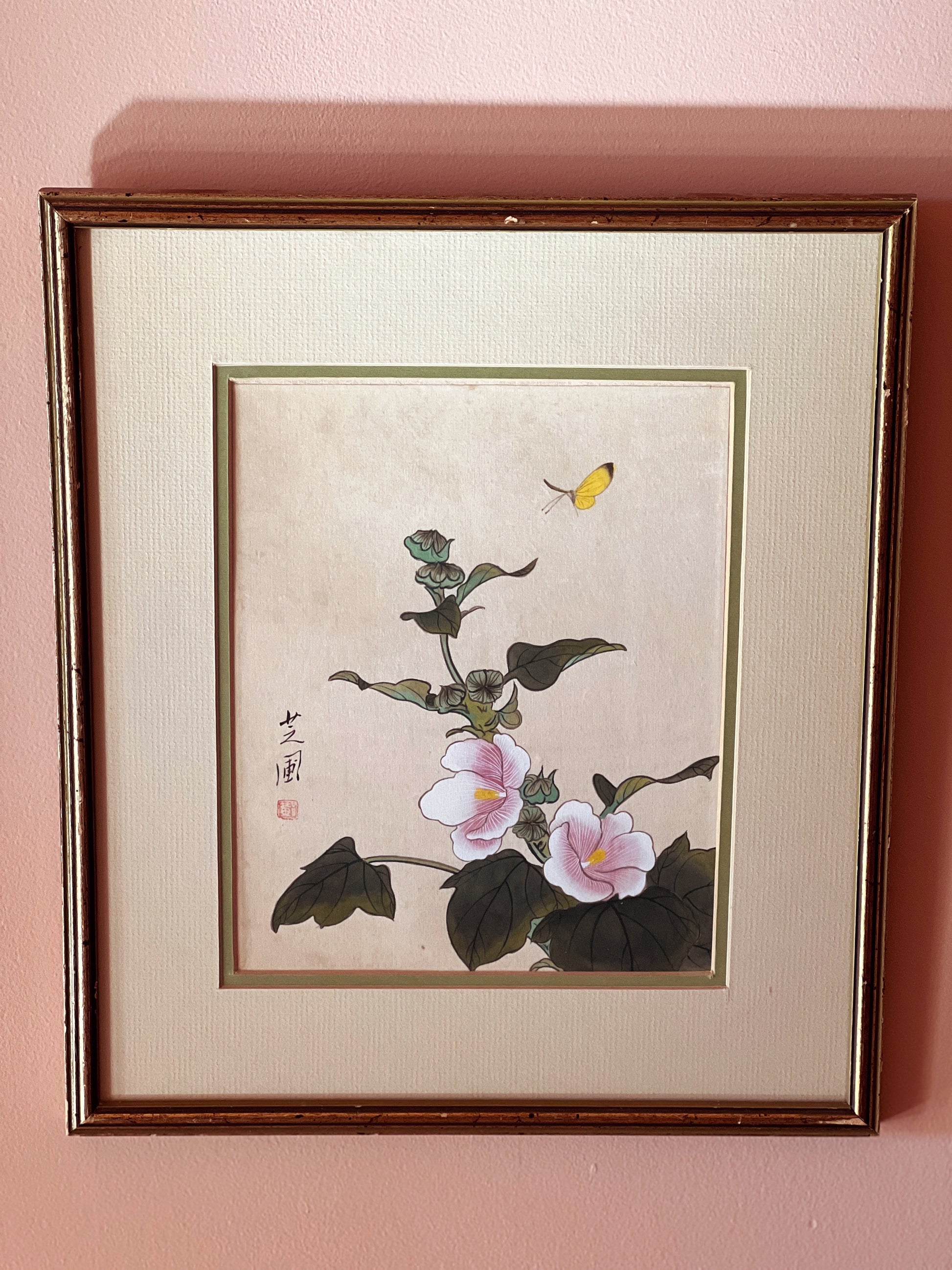 Framed artwork of flowers and a butterfly on a pink wall