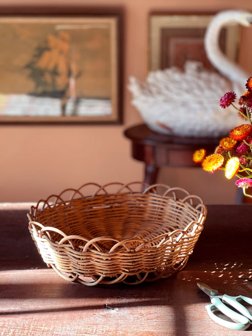Wicker basket on a wooden surface with a blurred background featuring a painting and flowers.