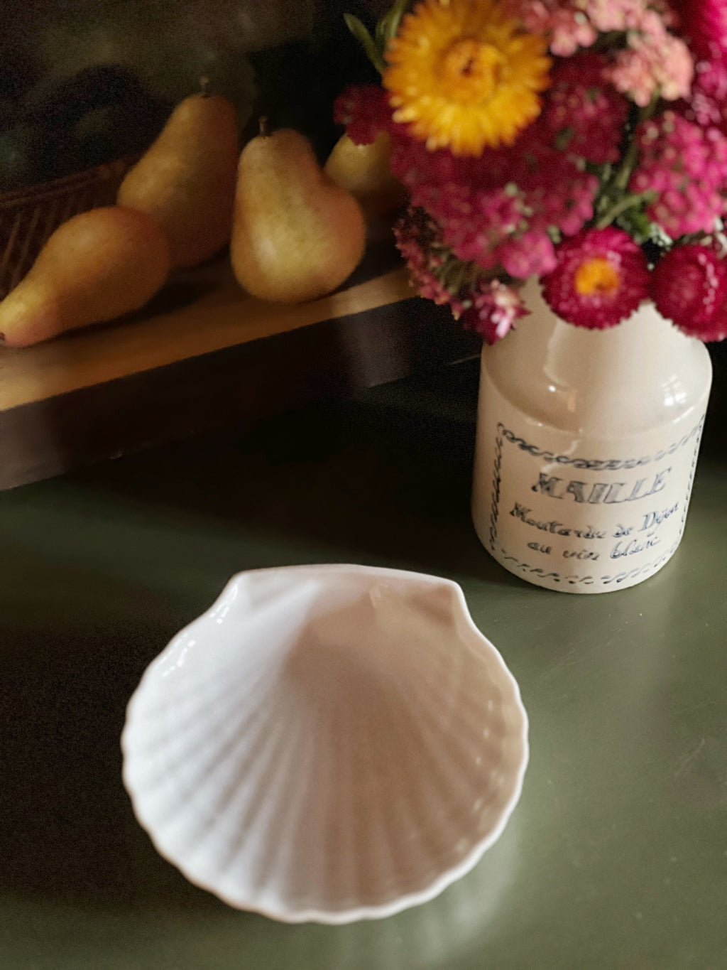 White shell on a dark surface with a vase of flowers in the background