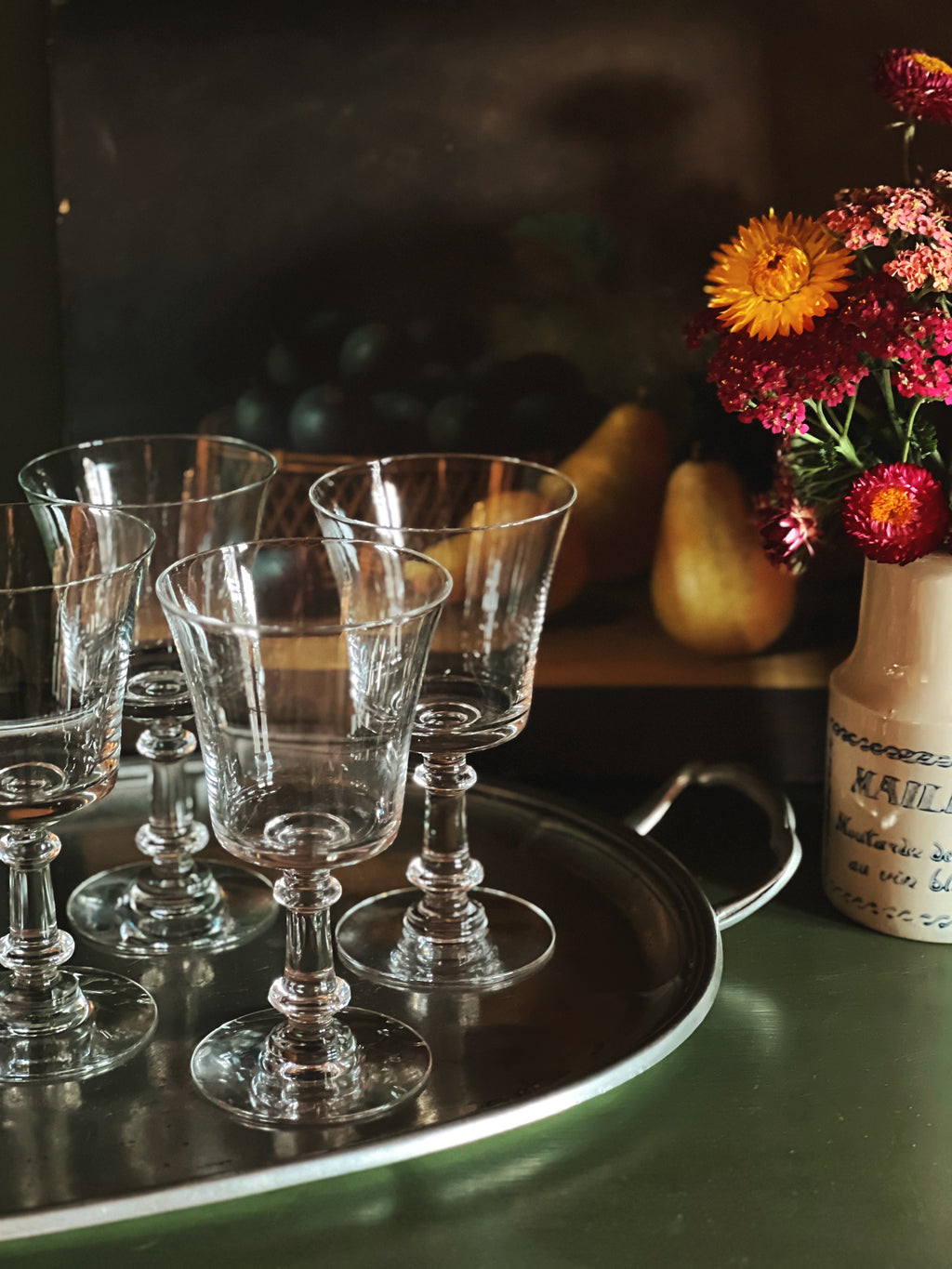 Set of clear glass goblets on a silver tray with a vase of flowers in the background.