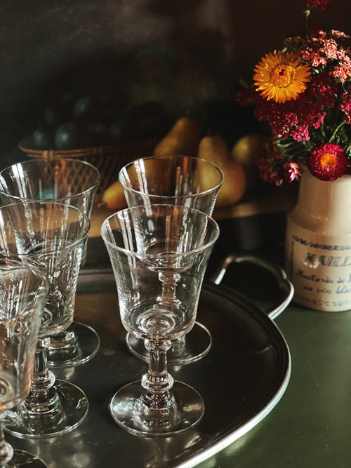 Set of clear glass goblets on a dark tray with a floral arrangement in the background.