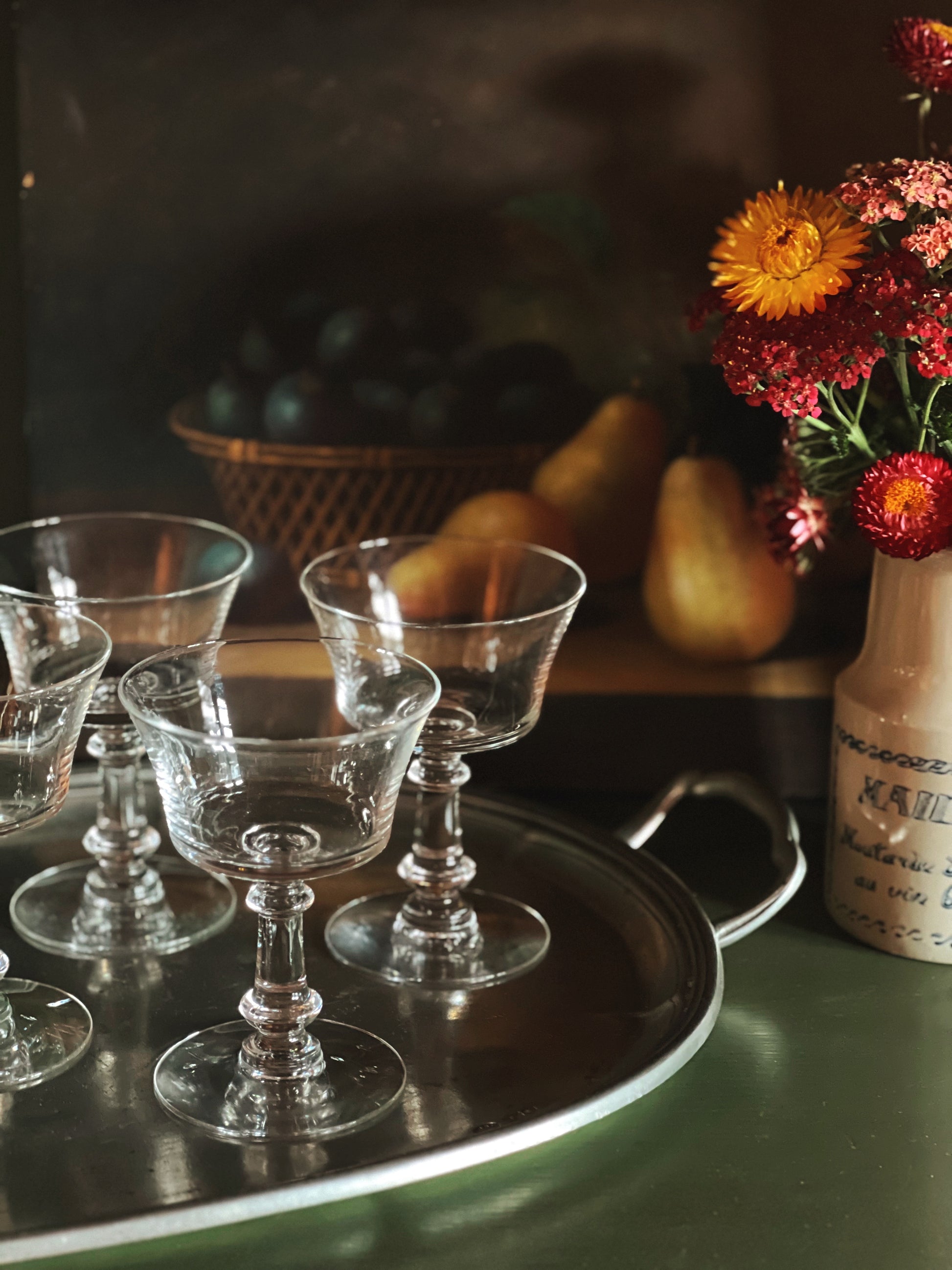 Clear glass goblets on a silver tray with a vase of flowers and fruit in the background.