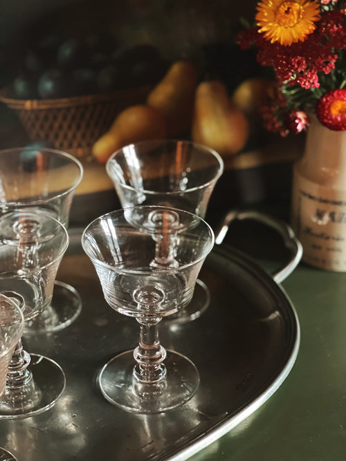Clear glass goblets on a metal tray with a blurred background of fruits and flowers.