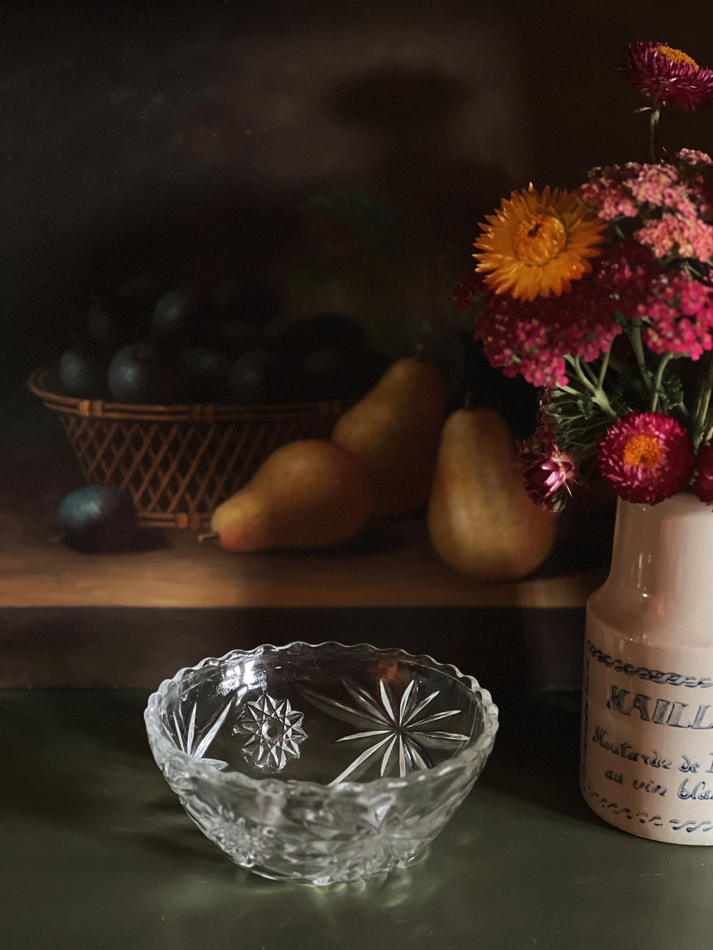 Still life with a glass bowl, pears, and flowers on a wooden surface.