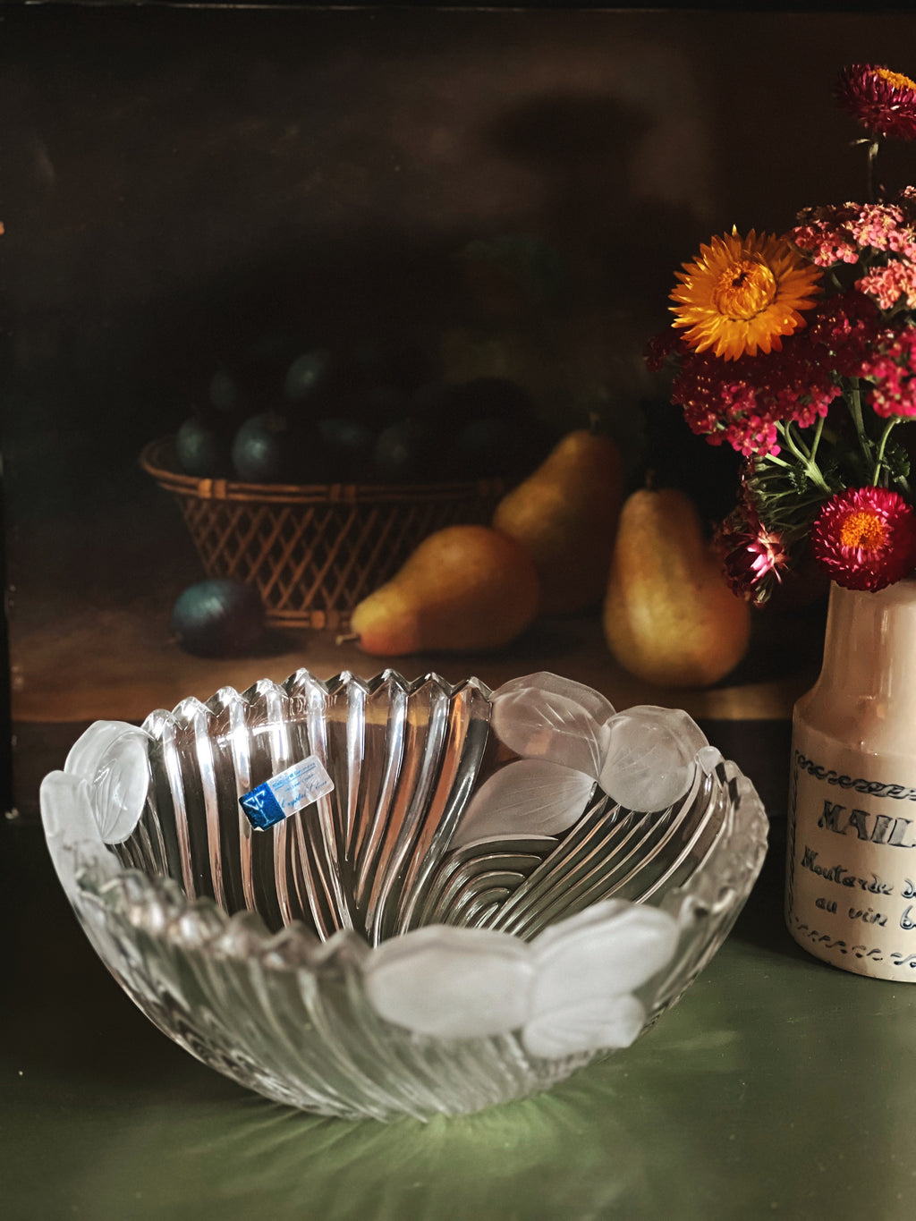 Clear glass bowl with silver spoons, pears, and flowers on a dark background