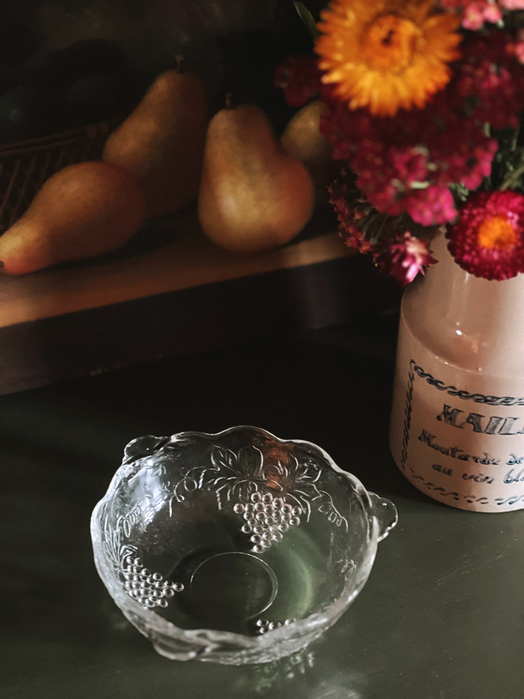 Decorative glass bowl on a dark surface with pears and flowers in the background