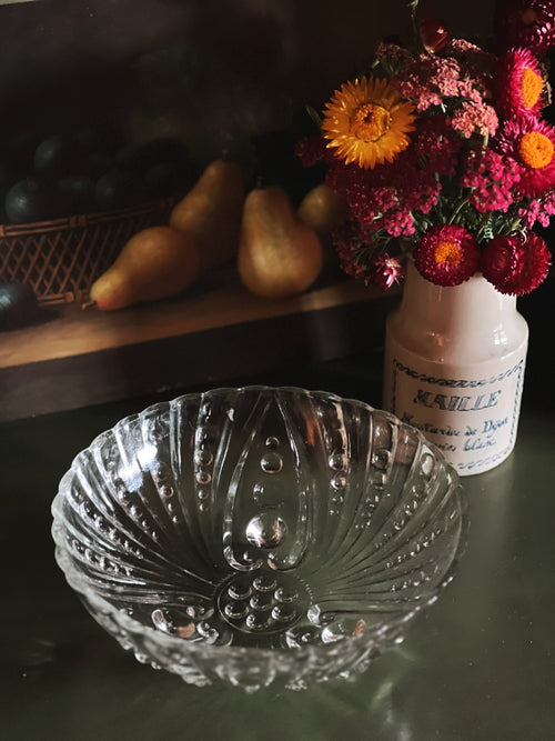 Clear glass bowl on a dark surface with a vase of flowers and pears in the background.