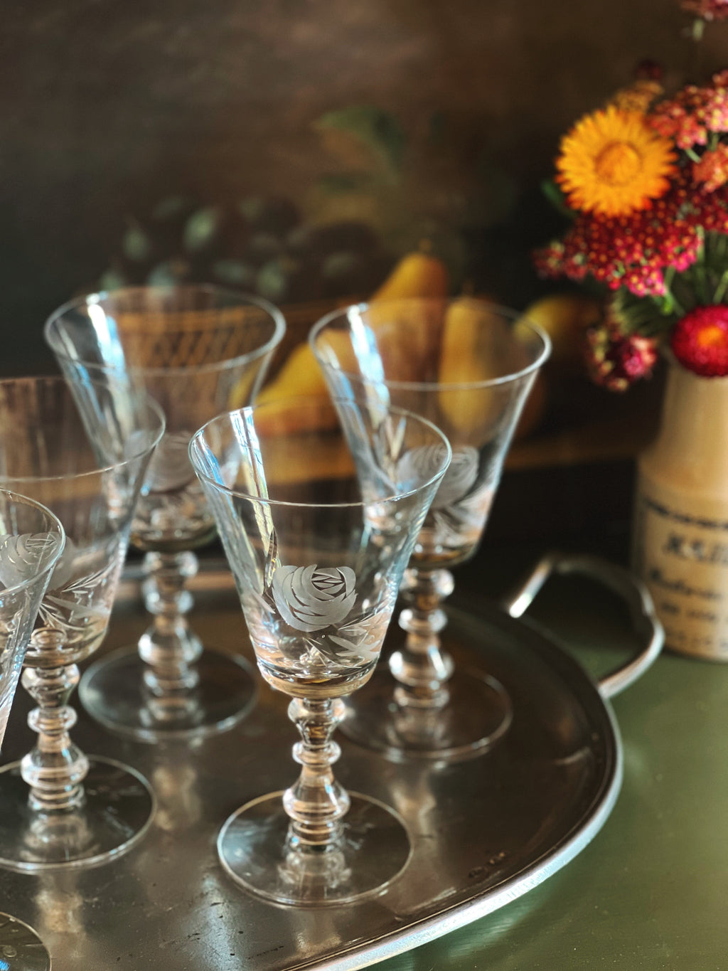 Set of crystal glasses on a silver tray with a floral arrangement in the background