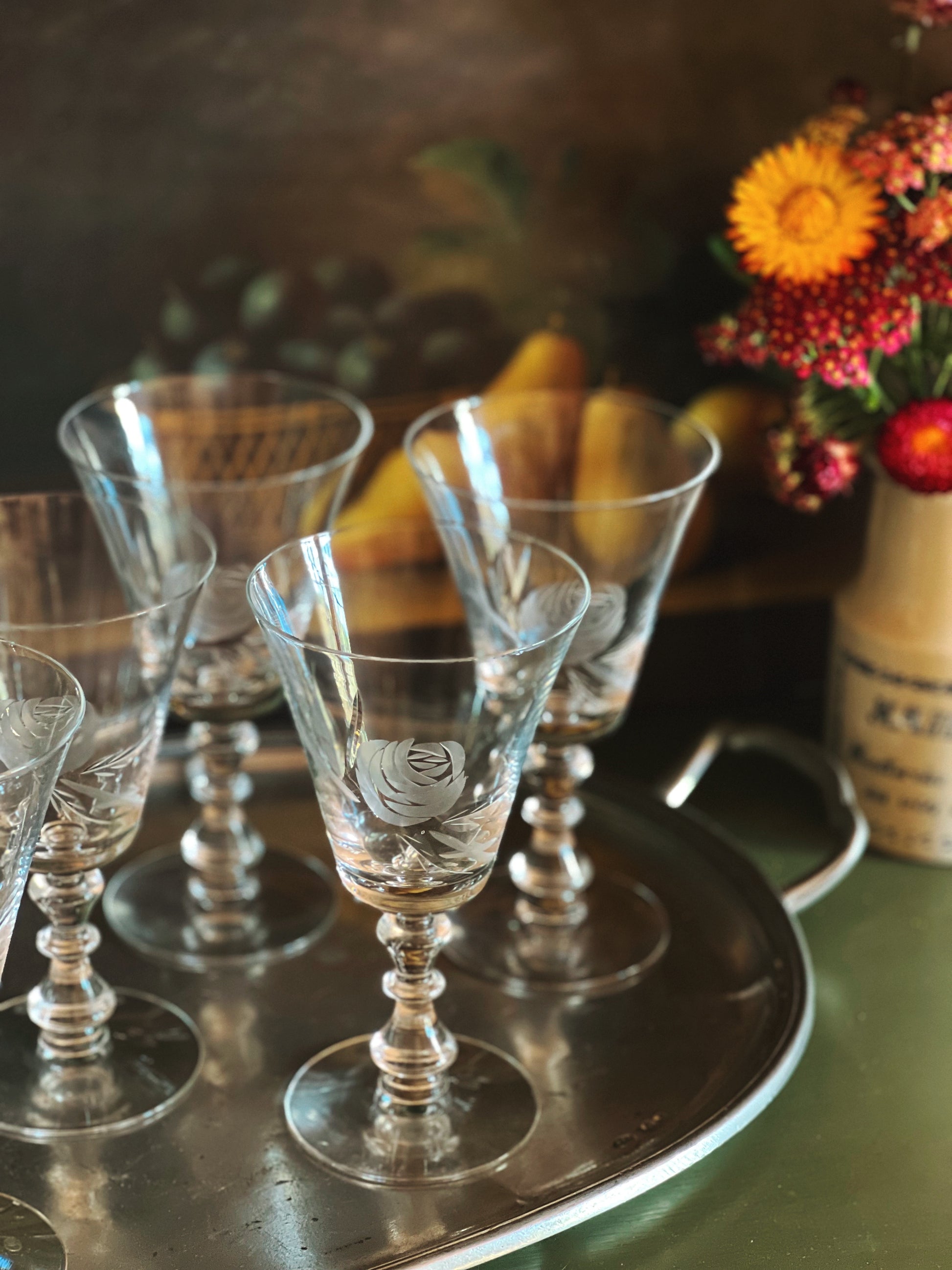 Set of crystal glasses on a silver tray with a floral arrangement in the background