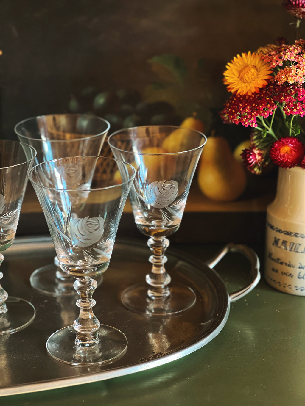 Set of decorative glass goblets on a tray with a vase of flowers in the background