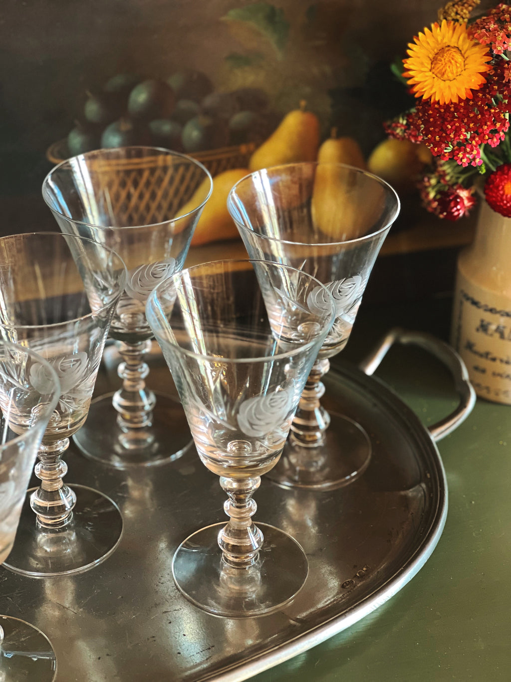 Set of clear glass goblets on a metal tray with fruits and flowers in the background