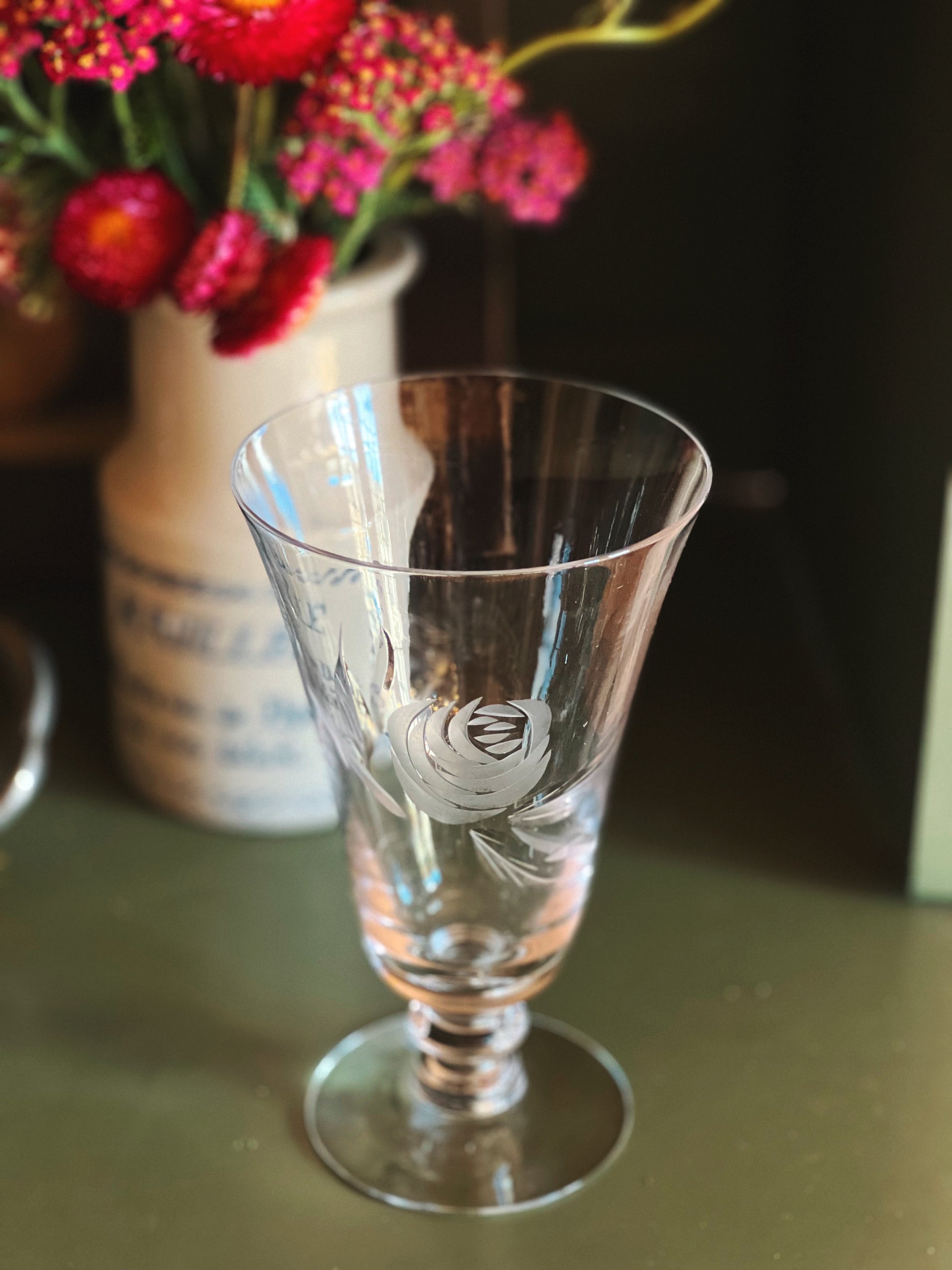Clear glass with intricate design on a table with flowers in the background