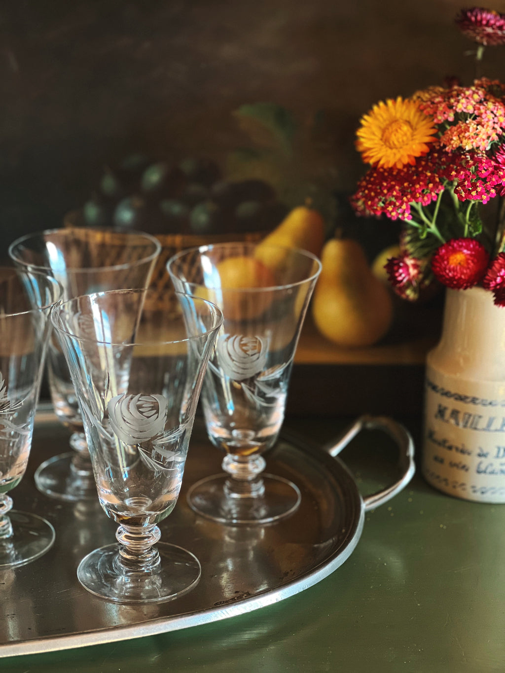 Clear glass goblets on a tray with fruits and flowers in the background