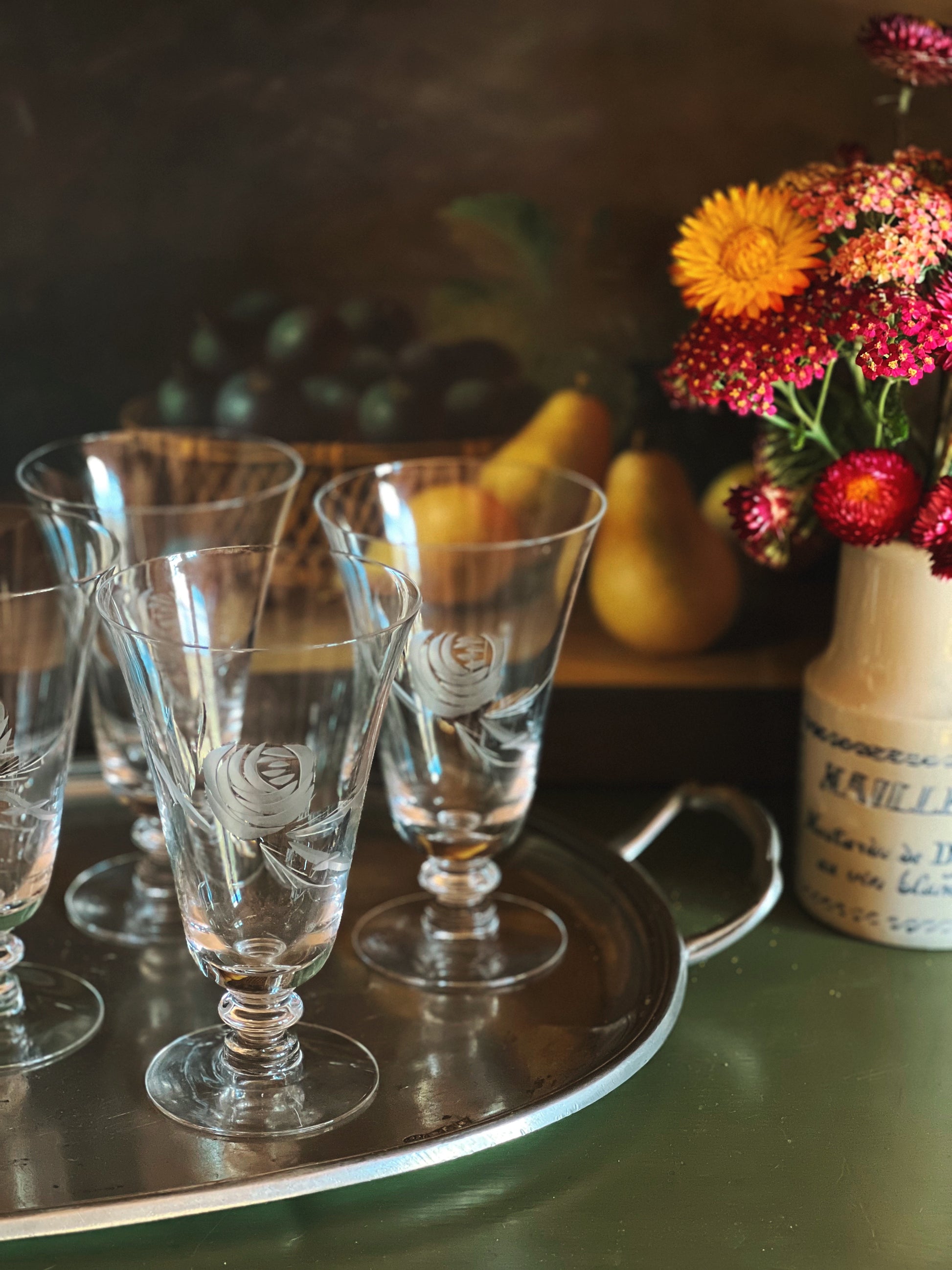 Clear glass goblets on a tray with fruits and flowers in the background