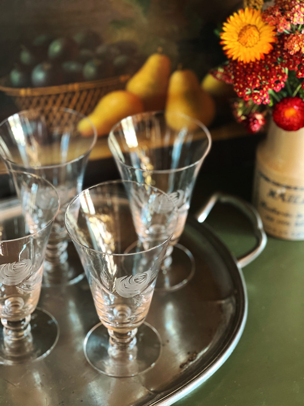 Set of etched glass tumblers on a metal tray with a decorative vase of flowers in the background.