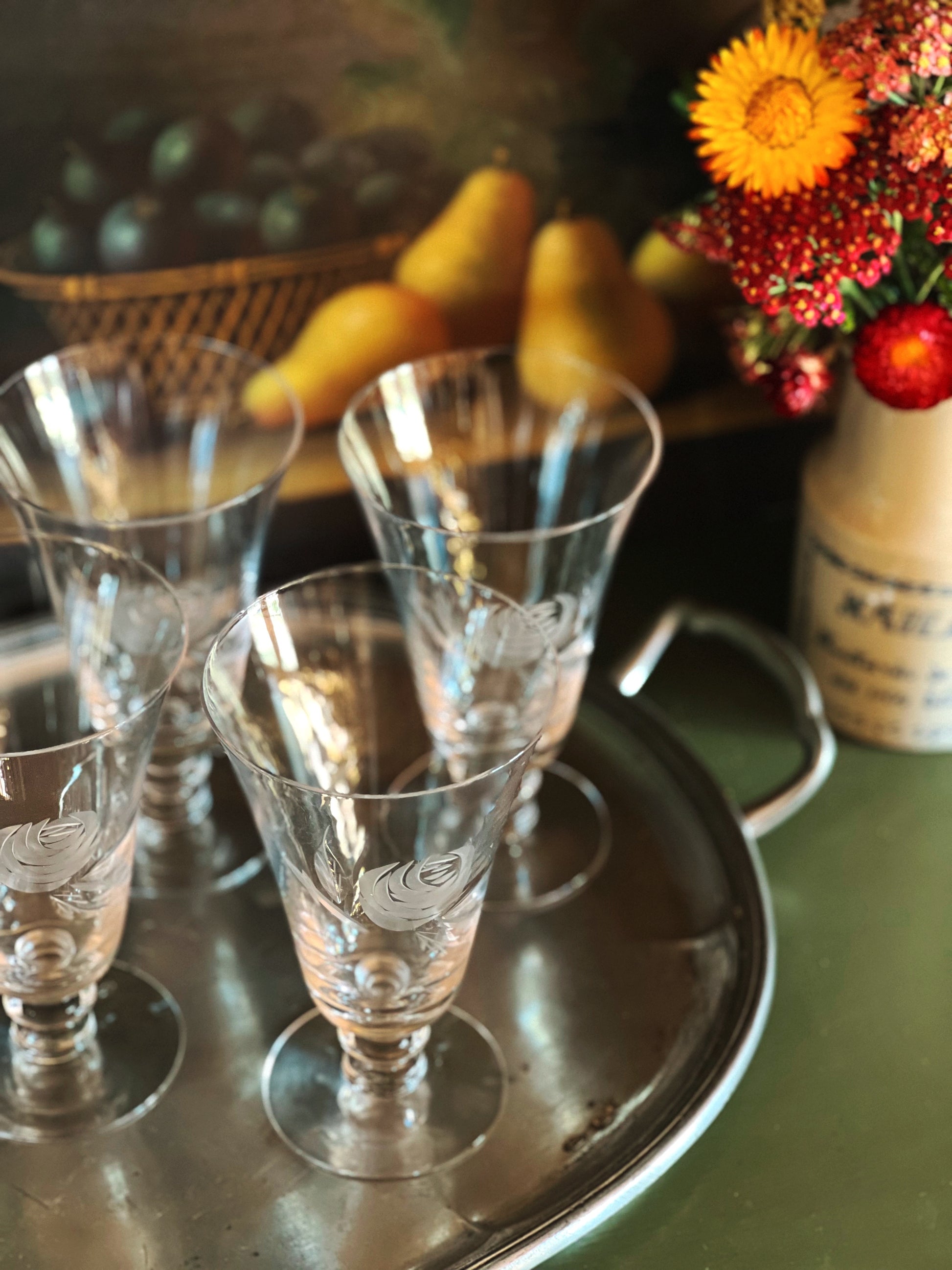 Set of etched glass tumblers on a metal tray with a decorative vase of flowers in the background.