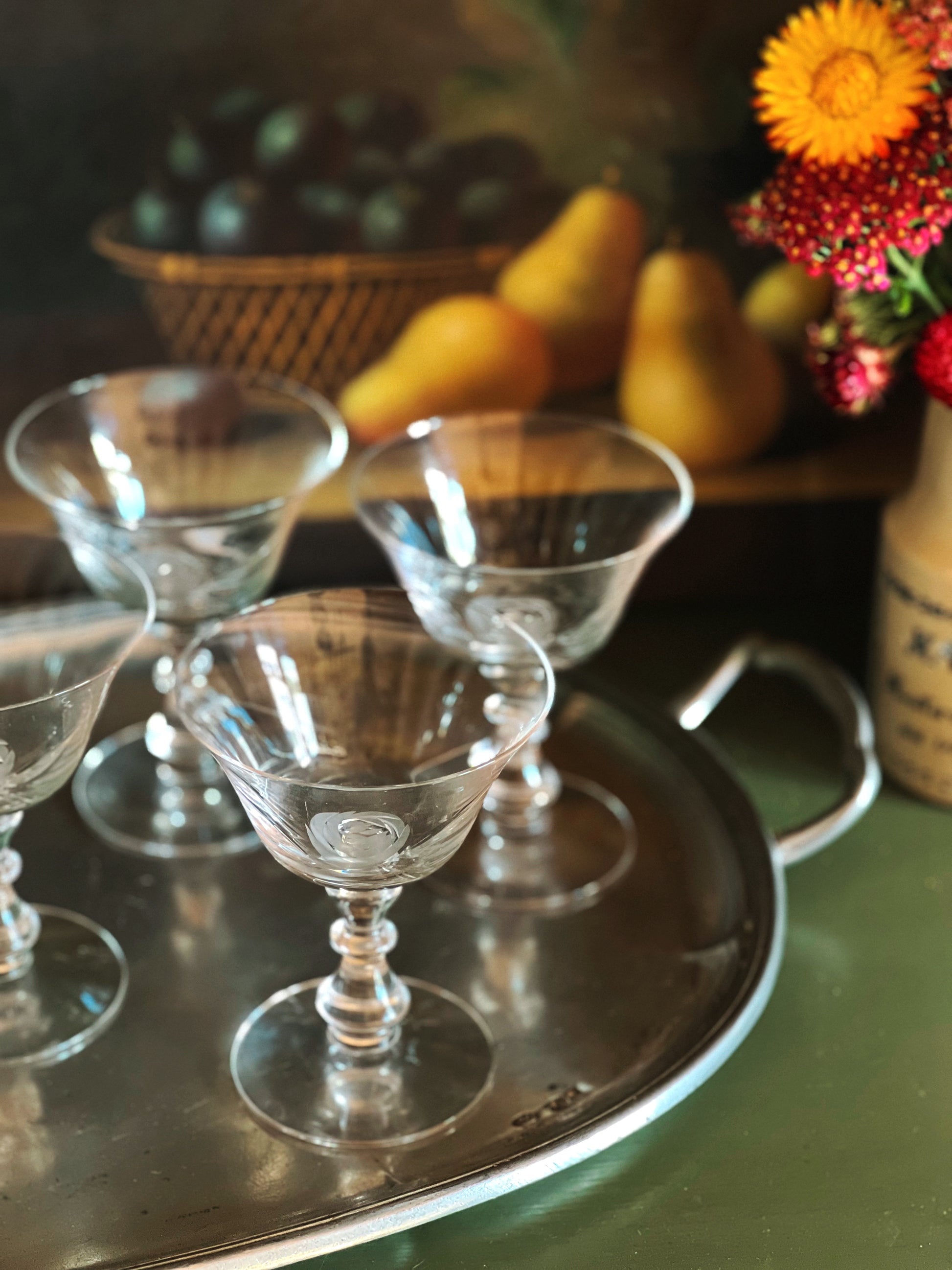 Clear glass goblets on a metal tray with fruits and flowers in the background