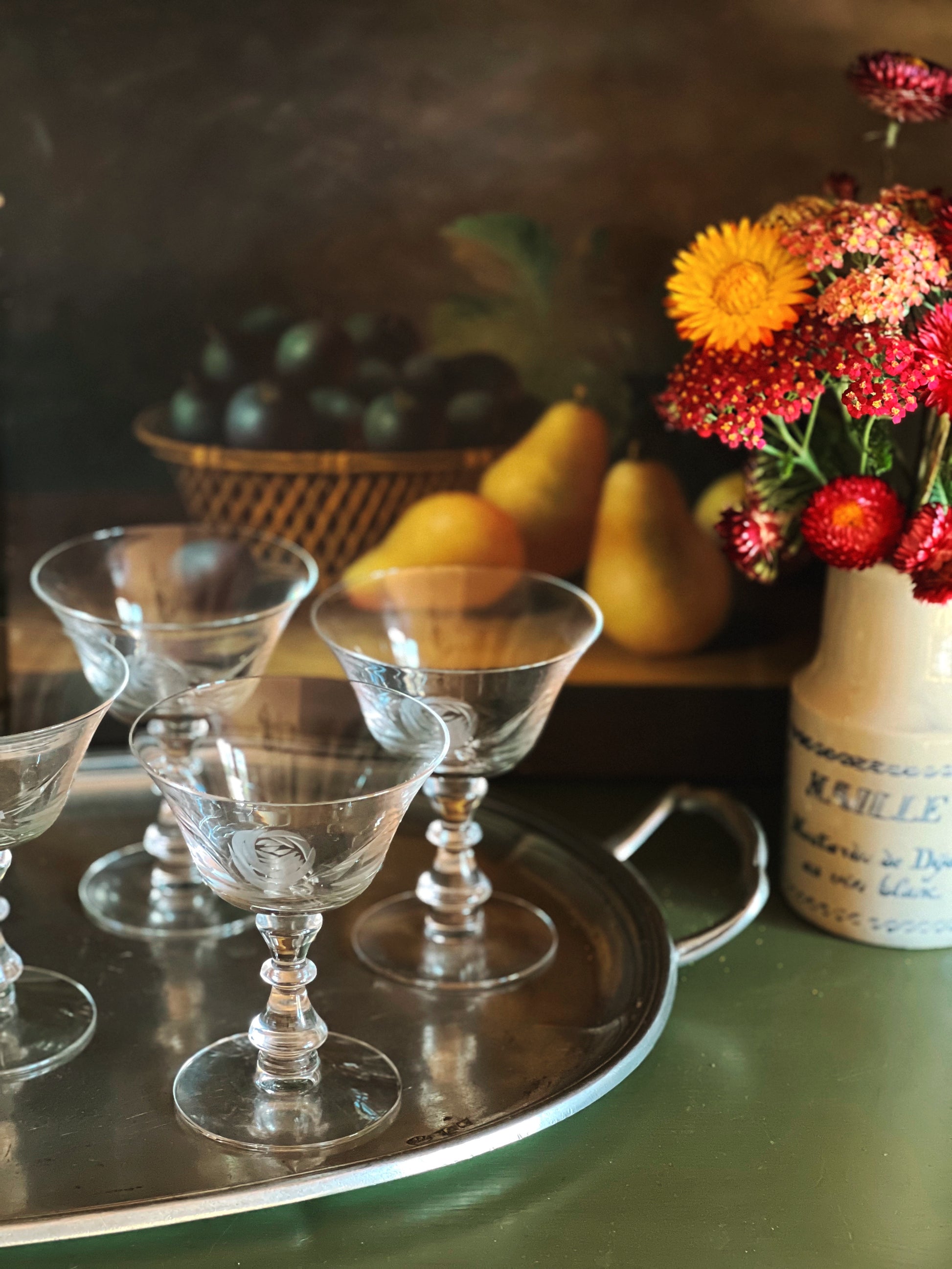 Set of glass goblets on a tray with fruits and flowers in the background