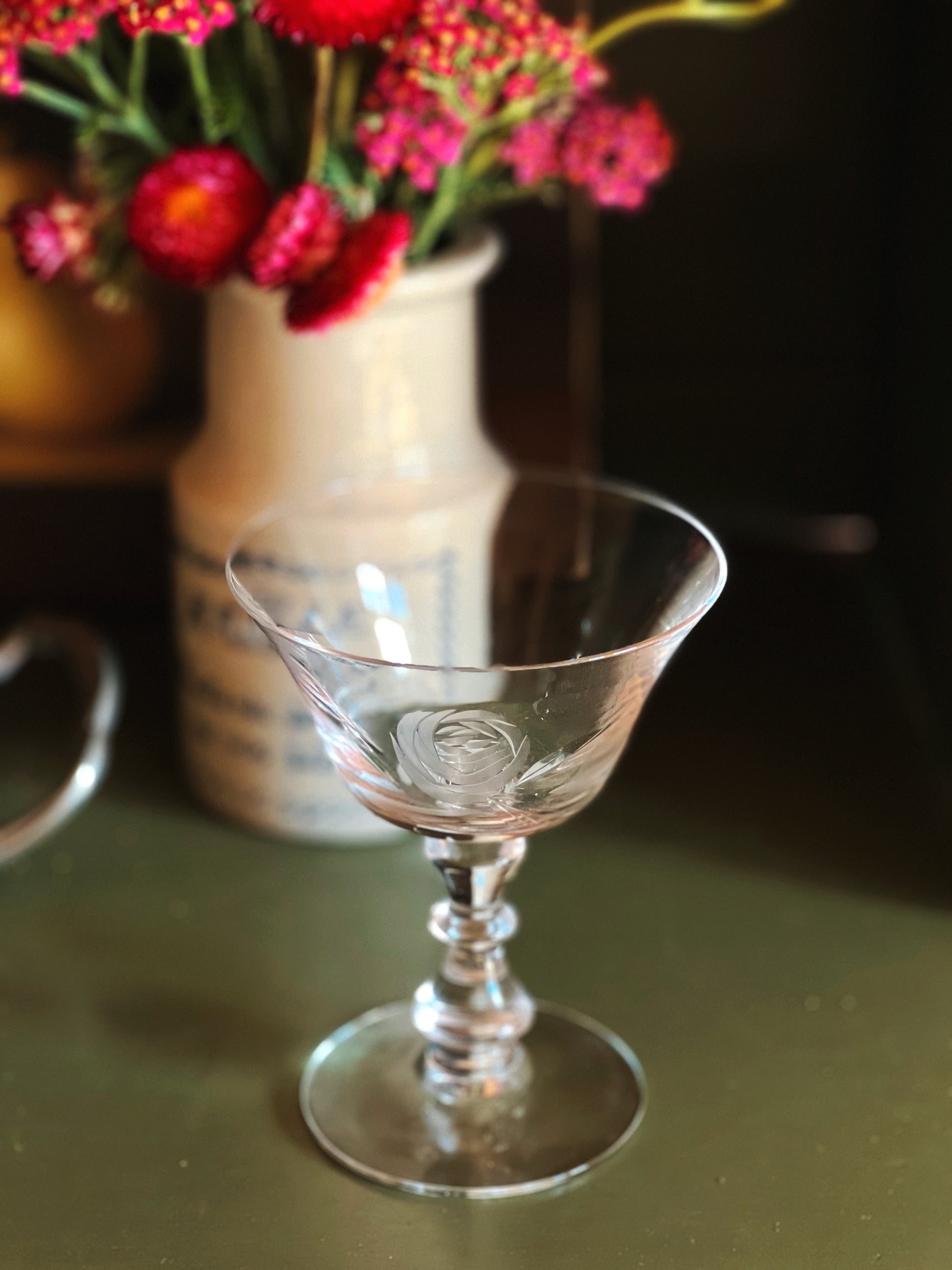Clear glass goblet on a reflective surface with flowers in the background