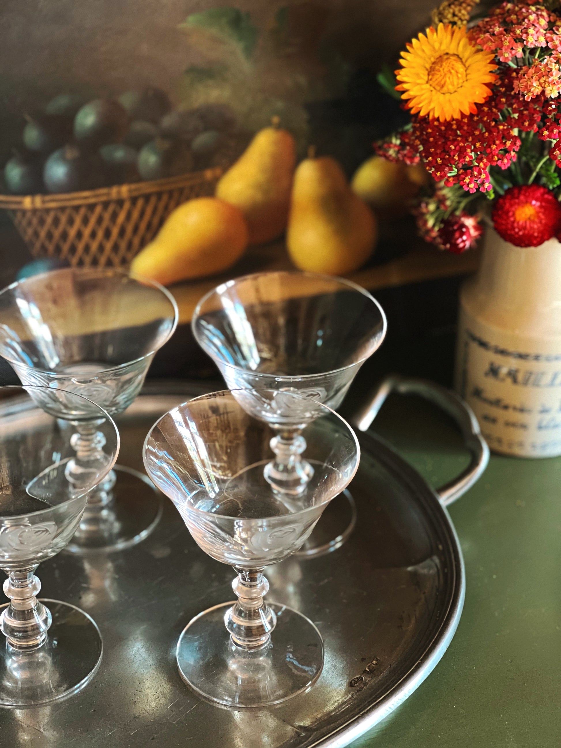 Clear glass goblets on a metal tray with fruit and flowers in the background