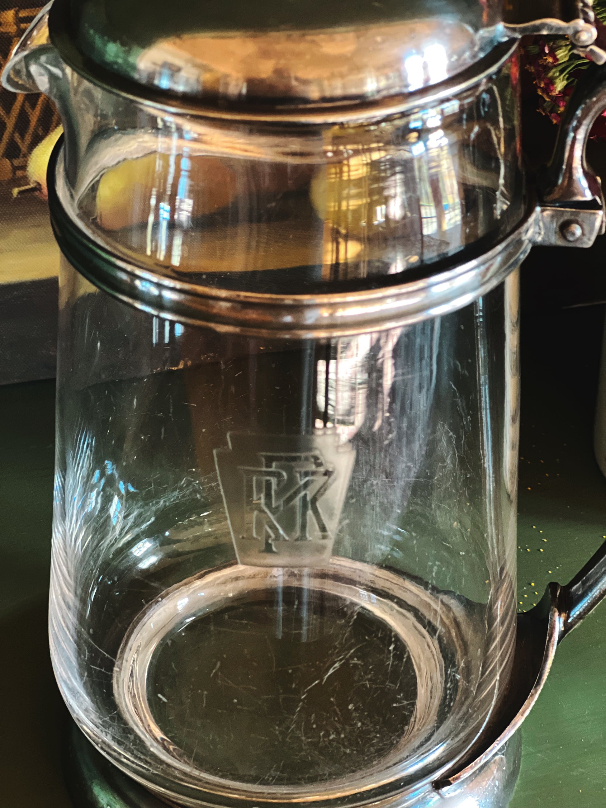 Clear glass pitcher with metal lid on a reflective surface