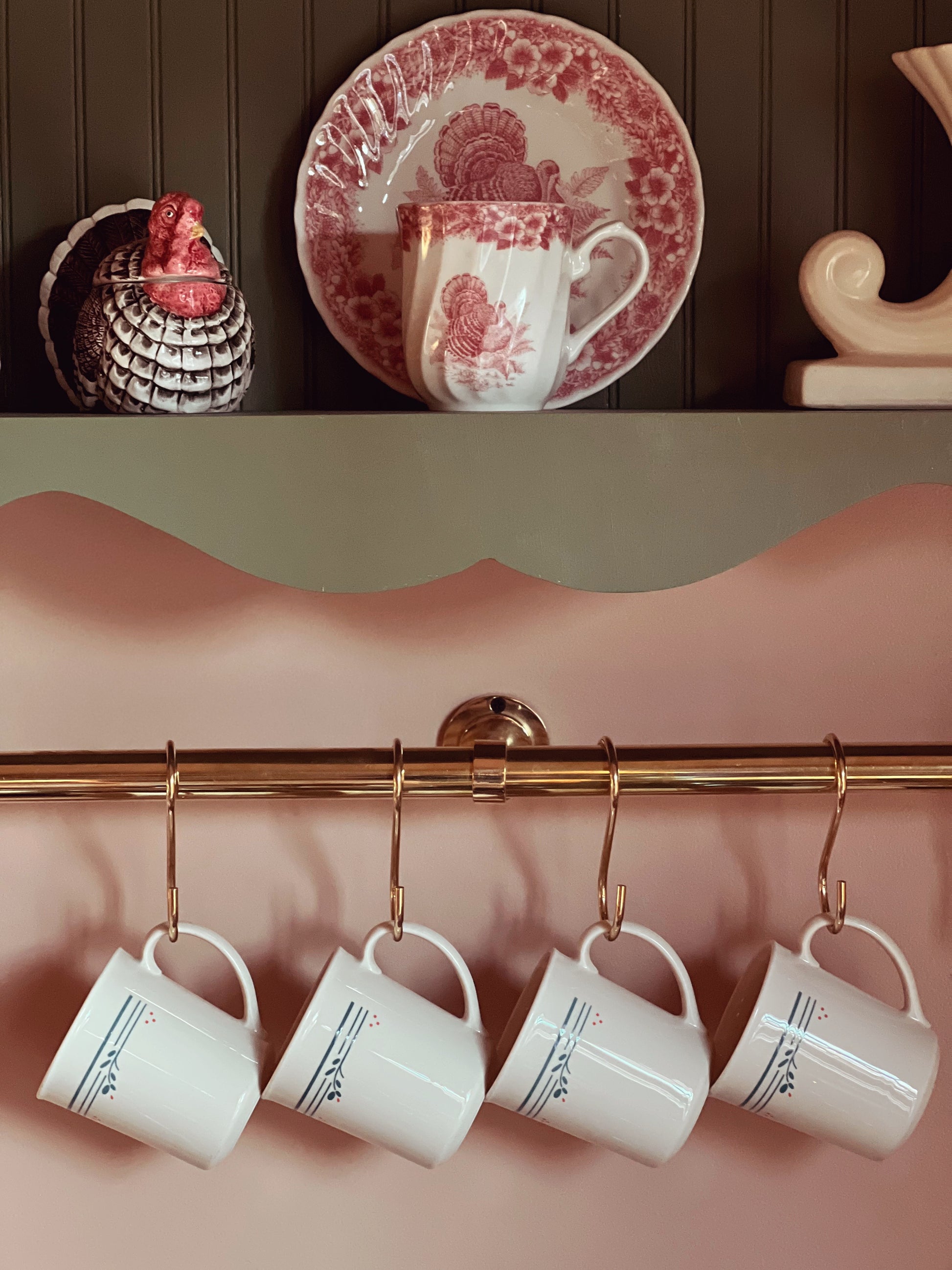 mugs hanging on a brass rod with a country shelf above