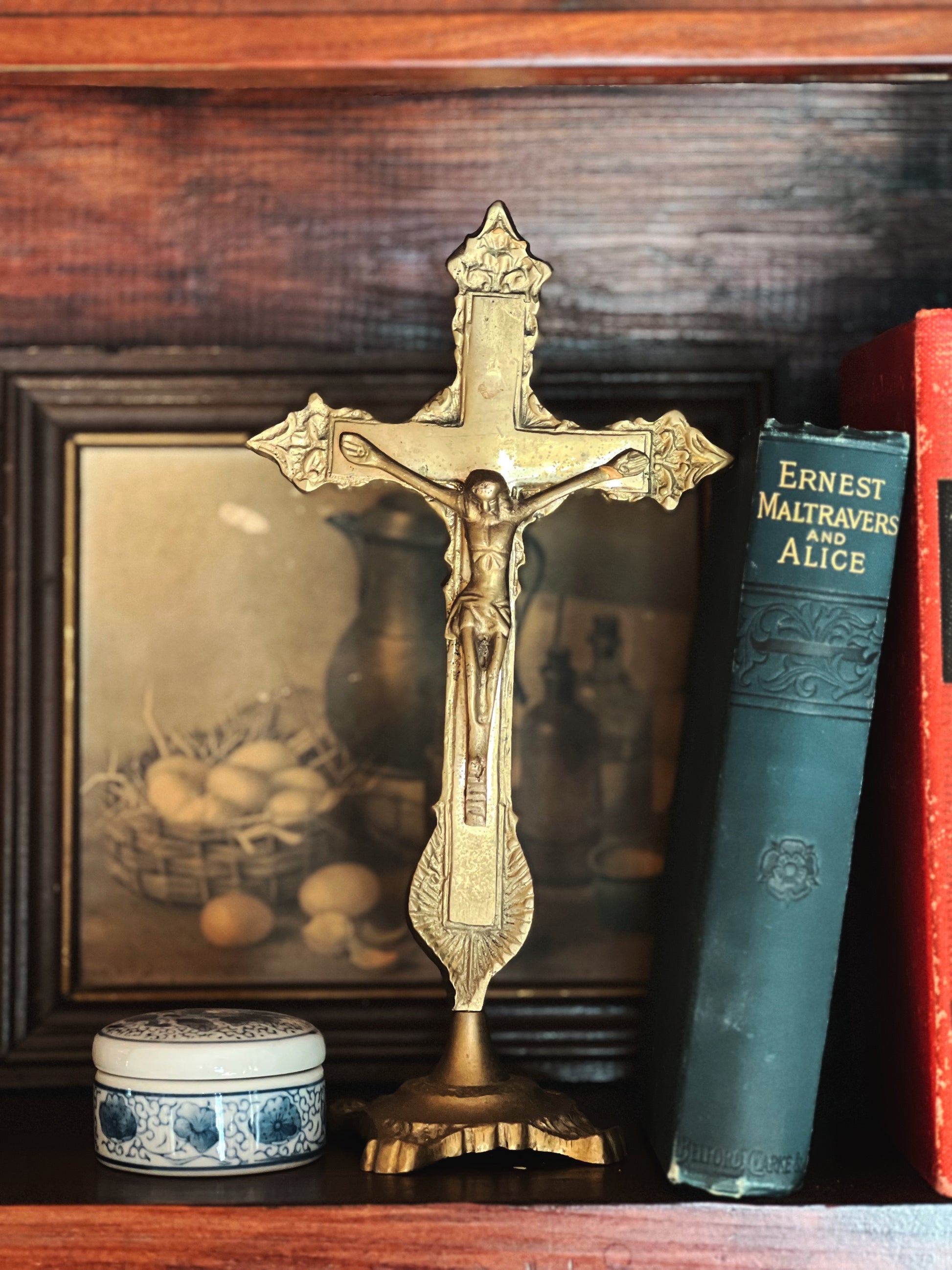 Decorative crucifix on a wooden surface with books and a painting in the background