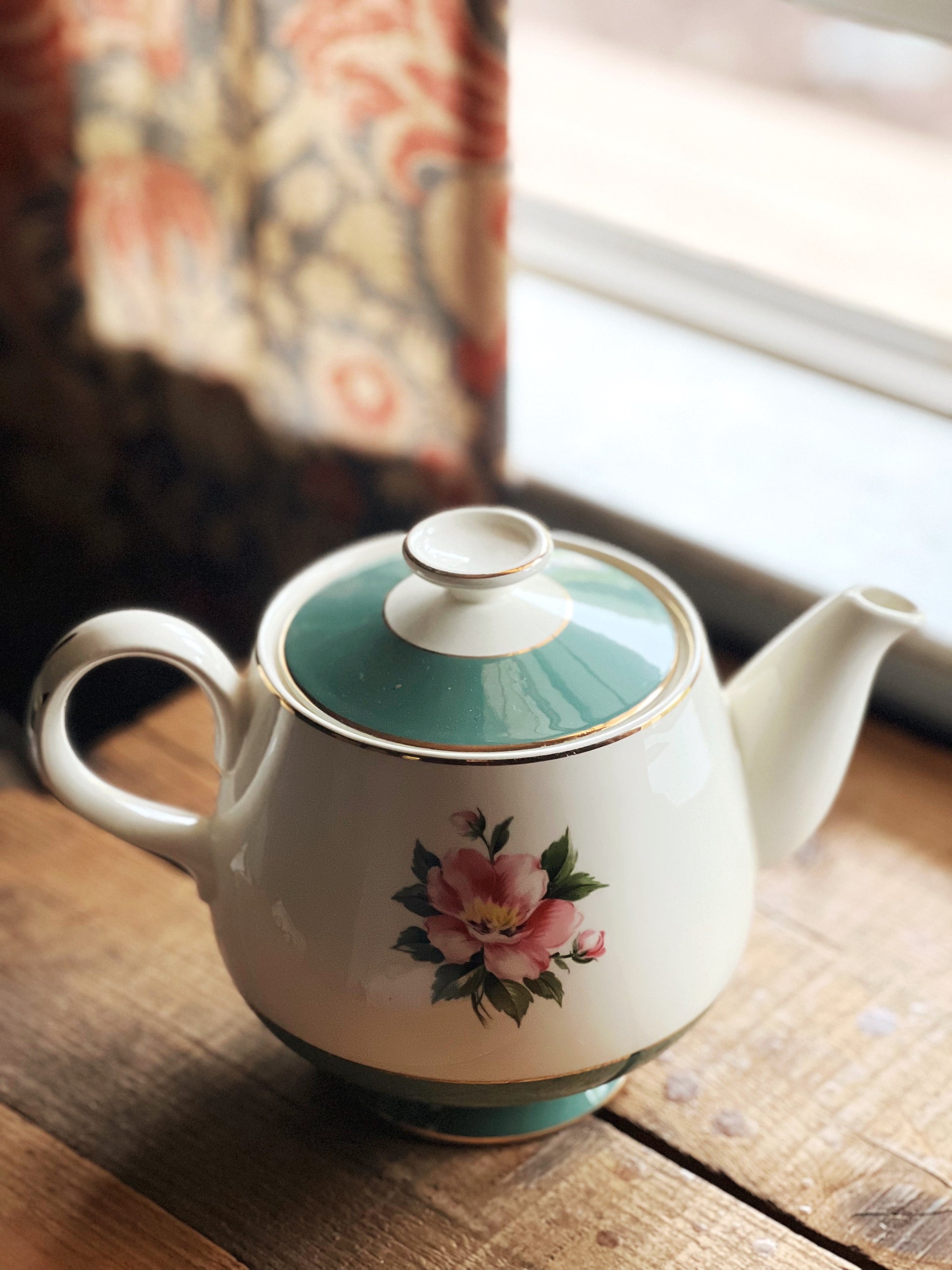 Teapot with floral design on a wooden surface near a window