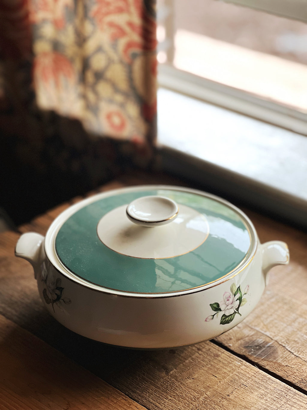 Ceramic pot with a green lid on a wooden surface near a window.