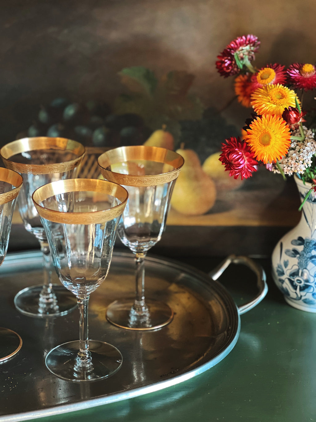 Decorative wine glasses with gold rims on a tray, accompanied by a vase of flowers.