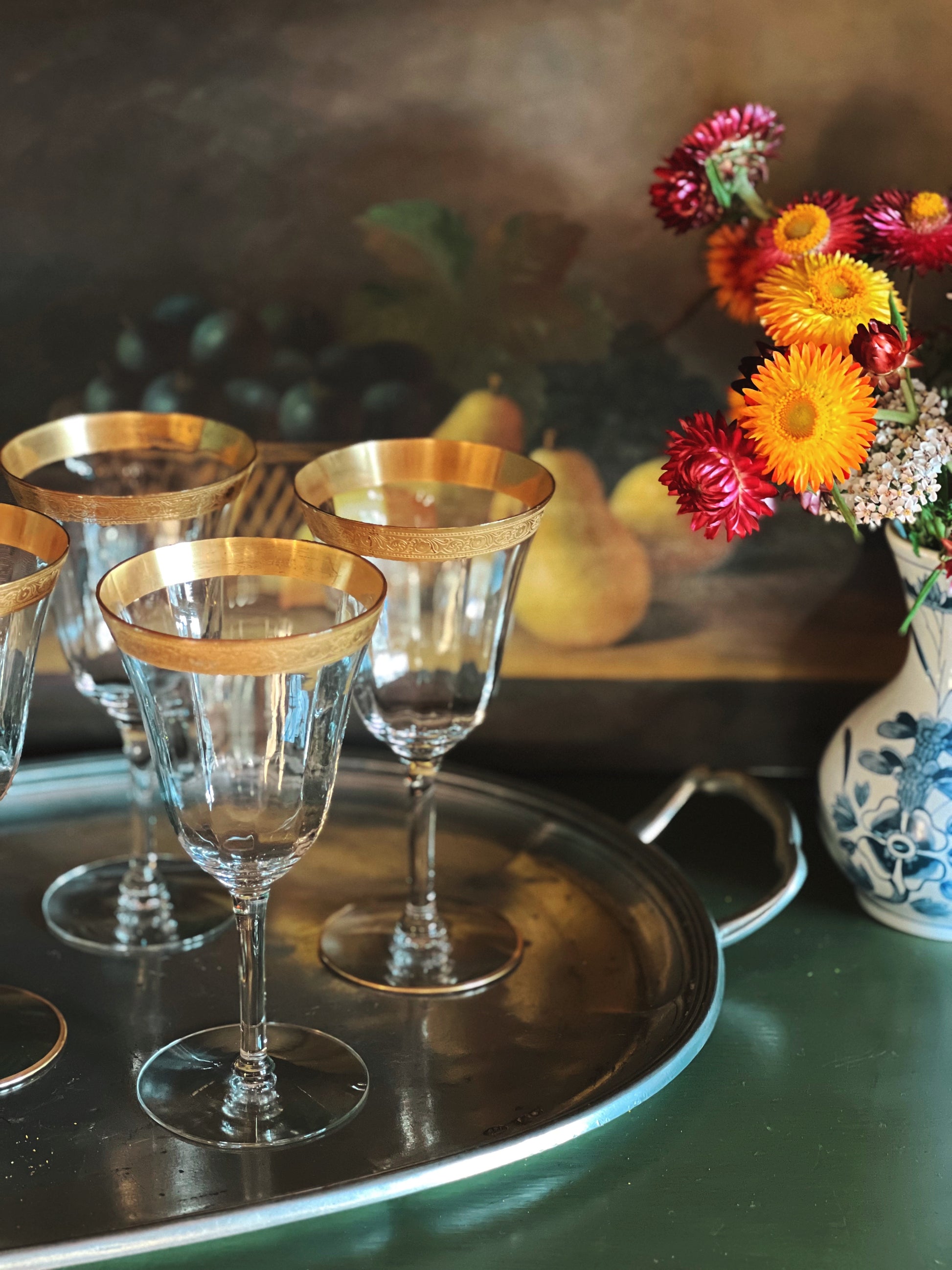 Decorative wine glasses with gold rims on a tray, accompanied by a vase of flowers.