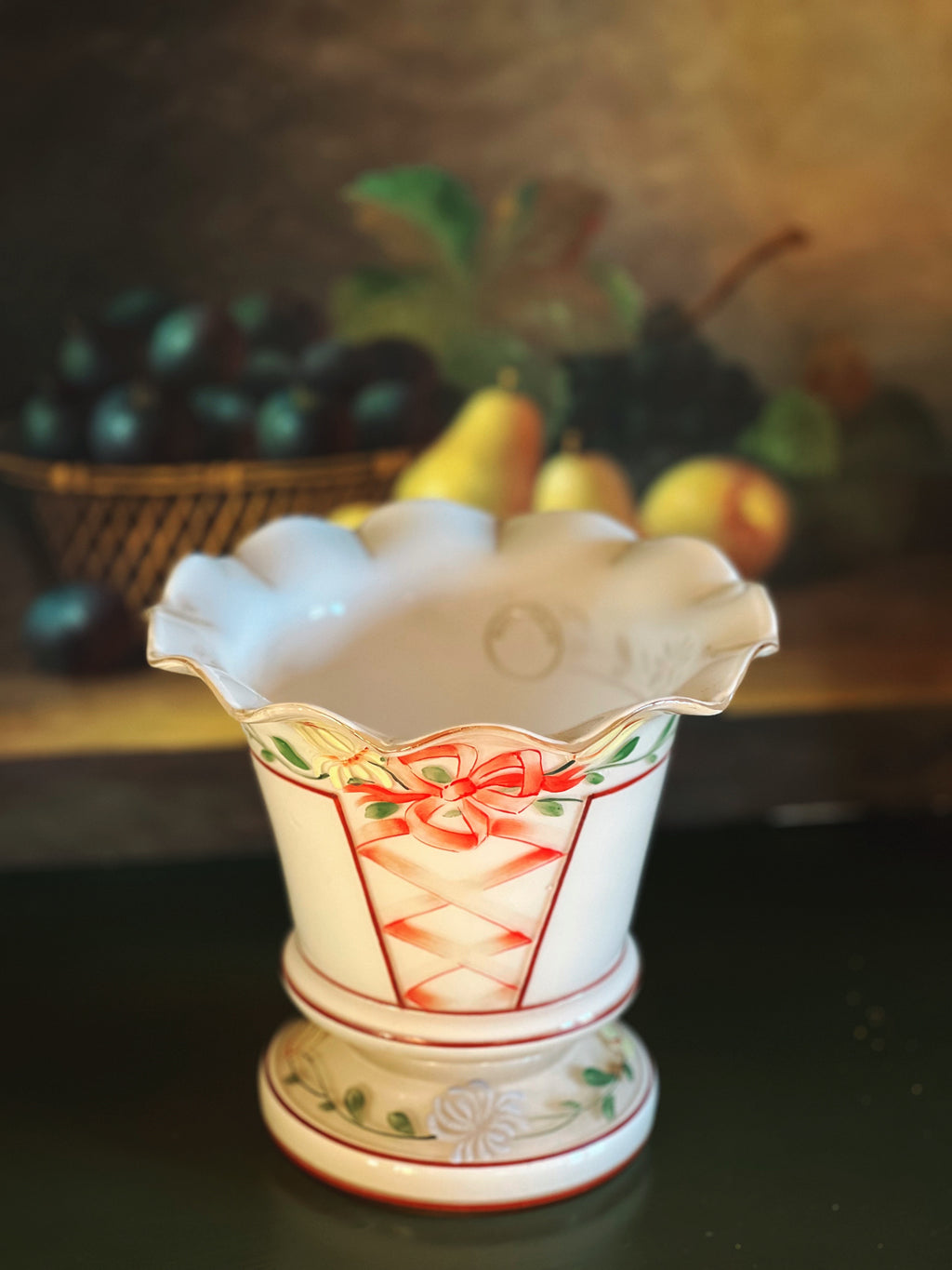 Decorative glass vase with floral design on a dark surface with fruit basket in the background