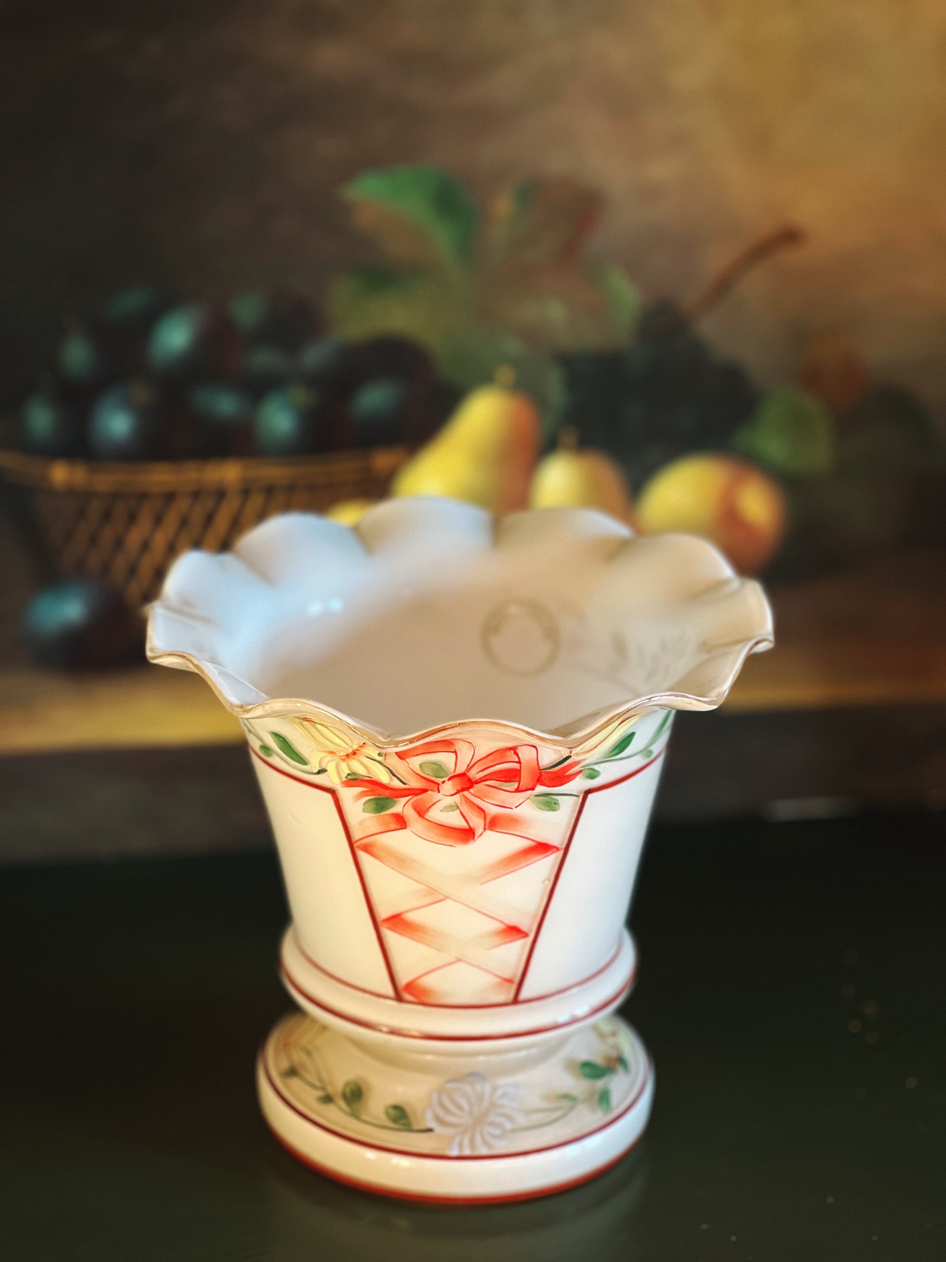 Decorative glass vase with floral design on a dark surface with fruit basket in the background