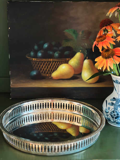 round silver butler's tray on a table next to a vase and a still life painting